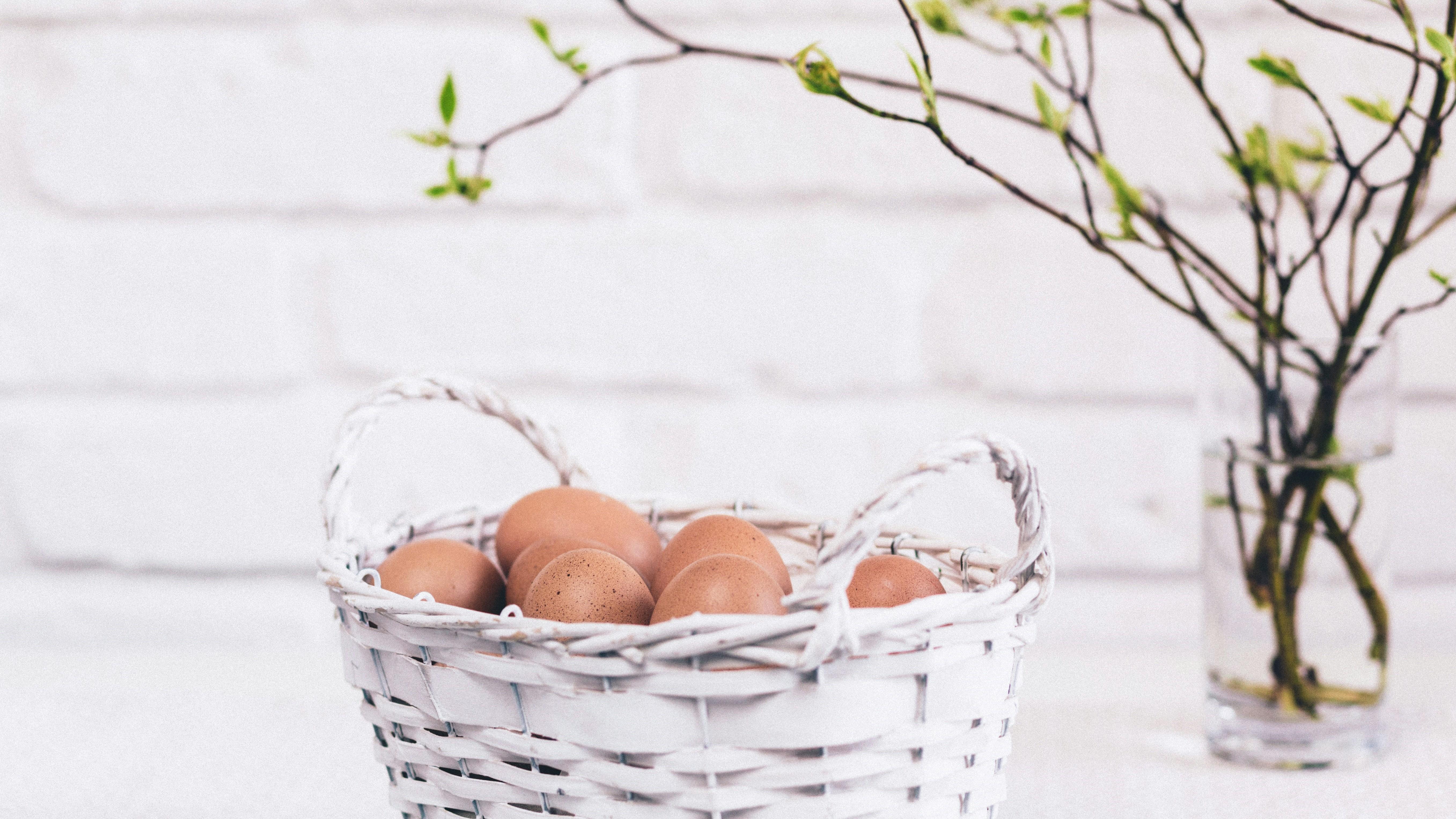 Ägg i en korg på en köksbänk. Bakom står en vas med påskris. 