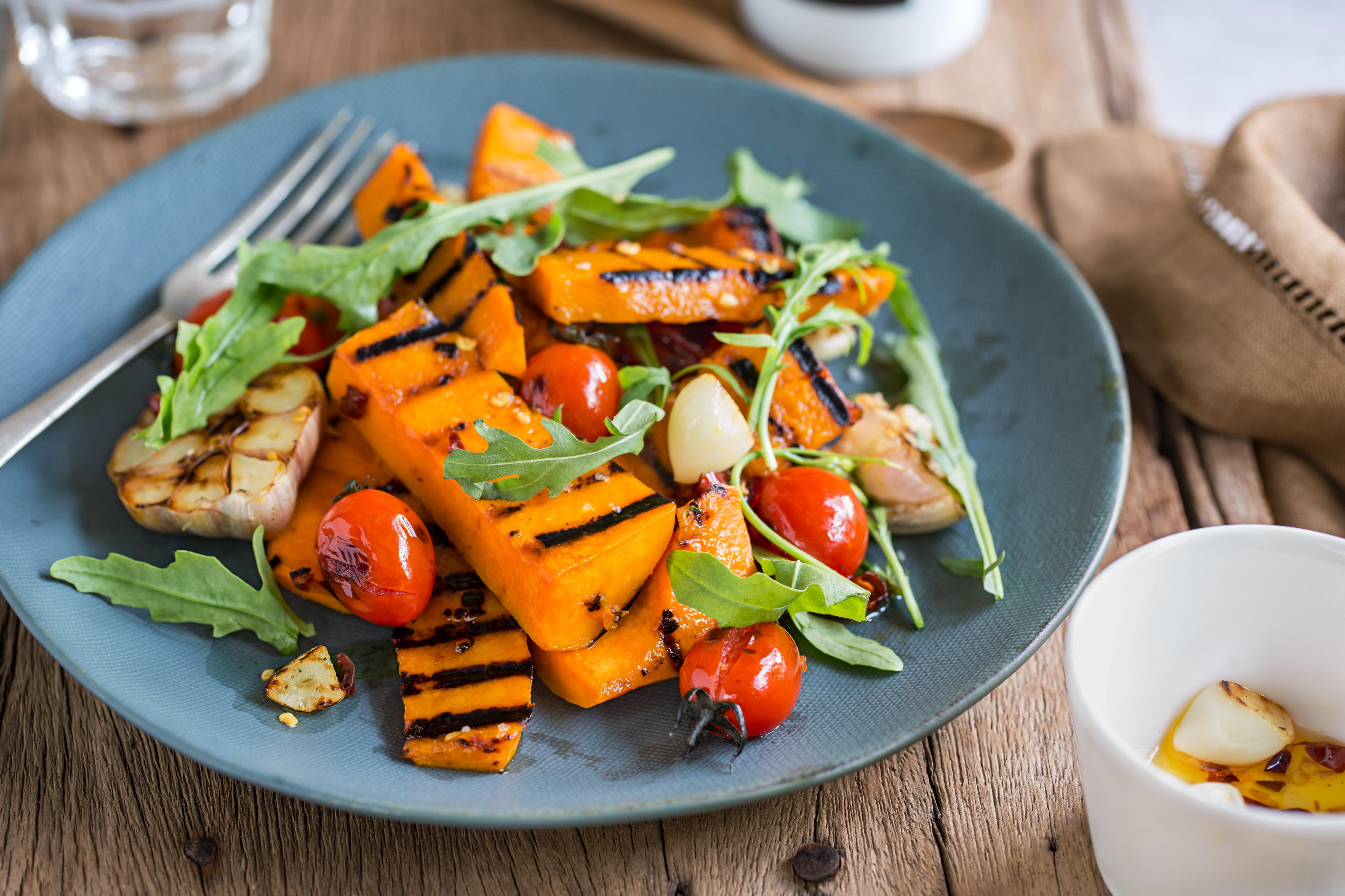 Blå tallerken med fargerik sommersalat med ruccola, småtomater og grillet gresskar. 