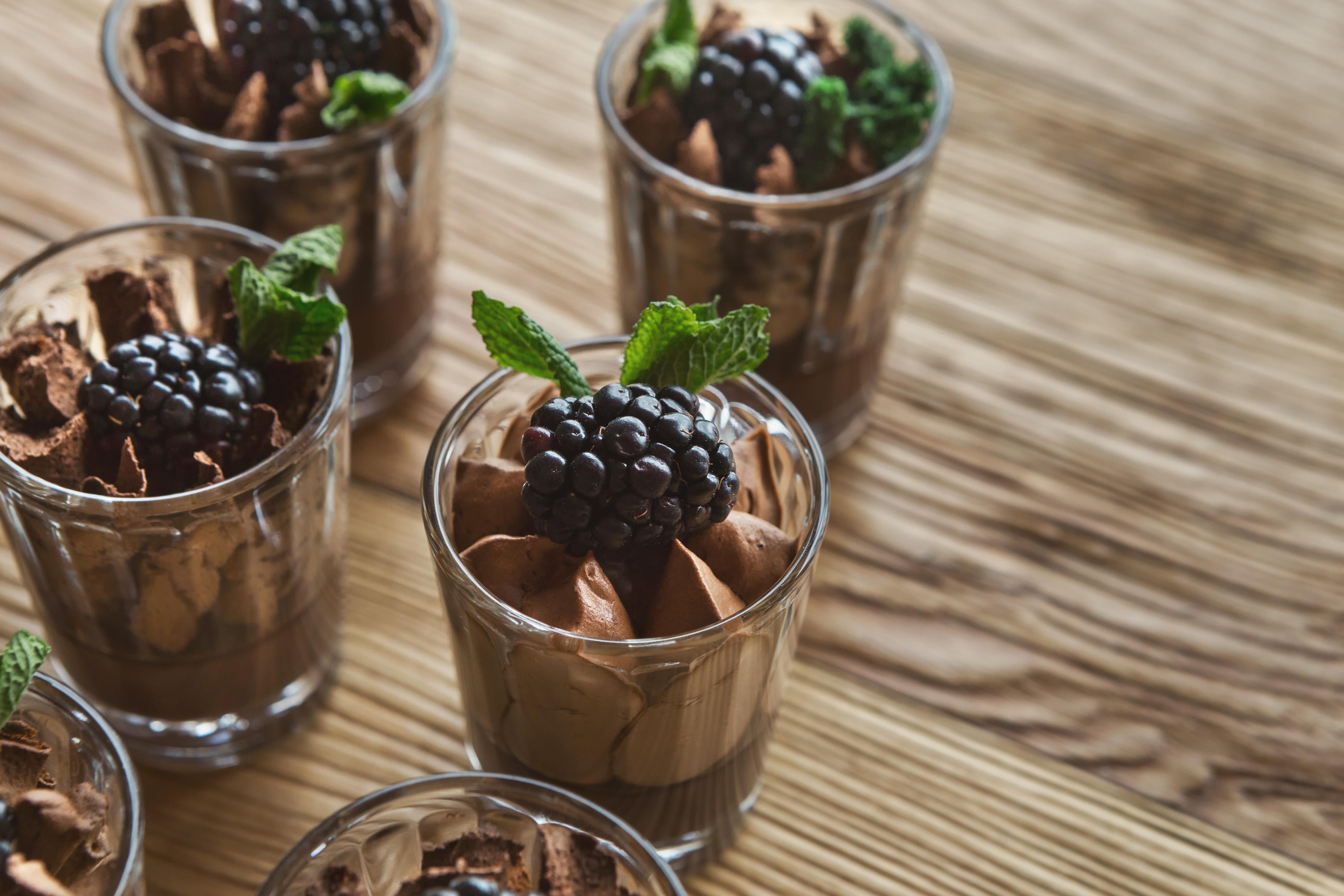 Seks glass med sjokolademousse på rekke. Pyntet med bjørnebær og mynteblader. 