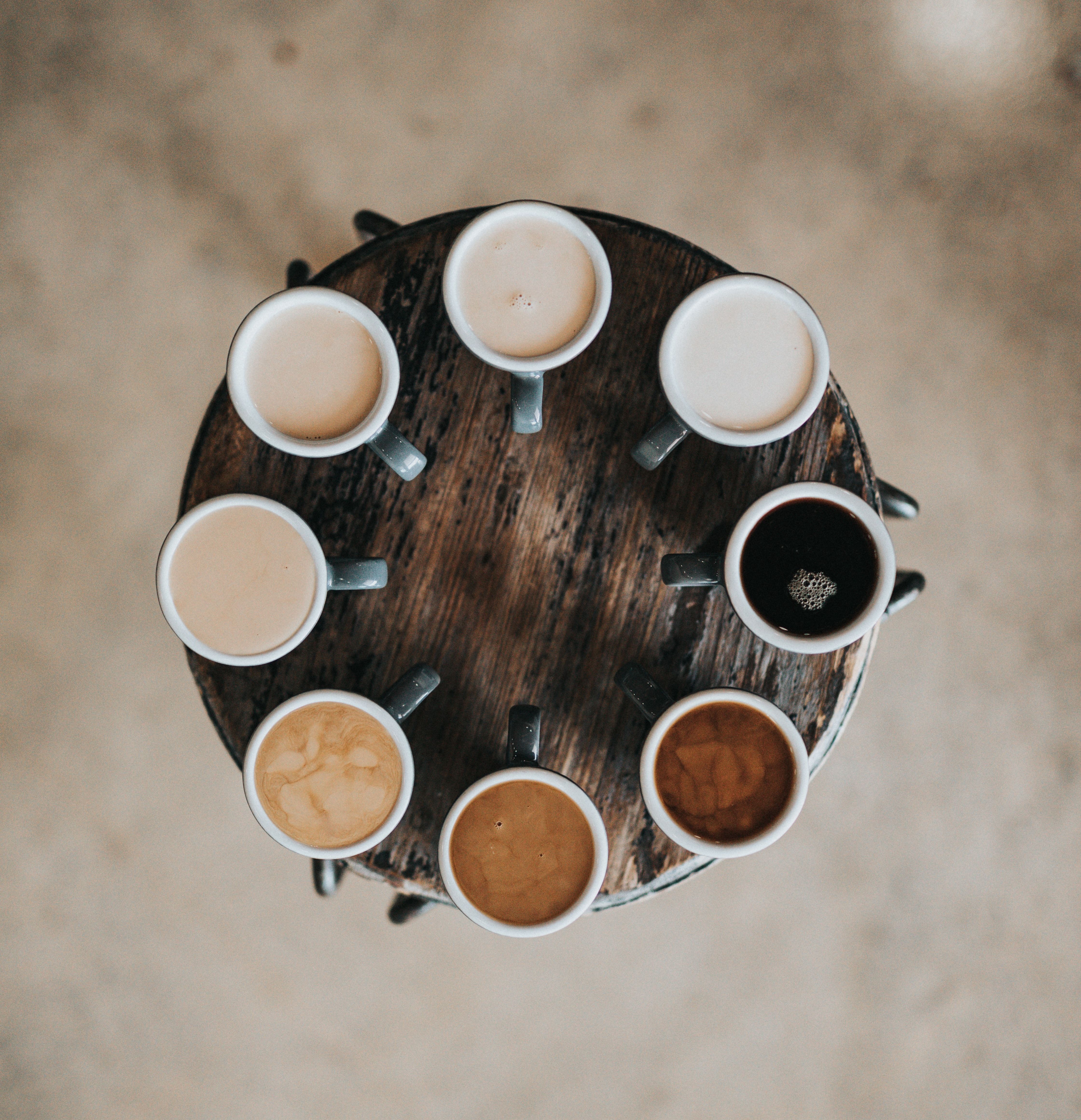 Kaffekopper med kaffe i hver sin nyanse plassert i sirkel på rundt bord 