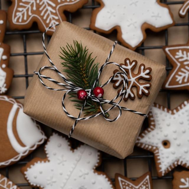 En julklapp på en plåt med glaserade pepparkakor. Paketet är pyntat med ett snöre, en pepparkaka och granbarr. 