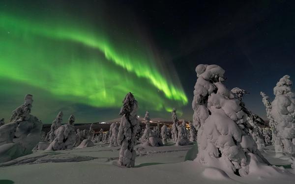 Bildet viser Finland med snødekte grantrær og nordlys.