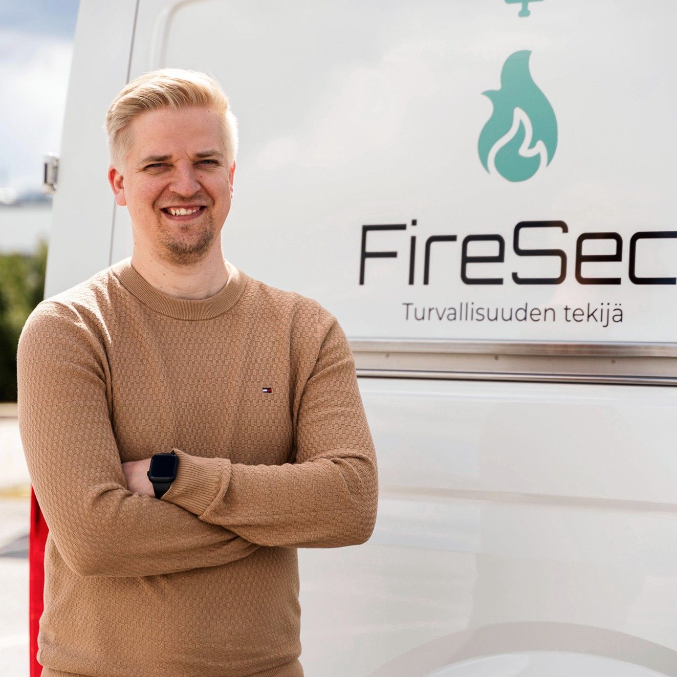 Hymyilevä mies seisoo hyötyajoneuvon edessä, jossa lukee teksti FireSec. 