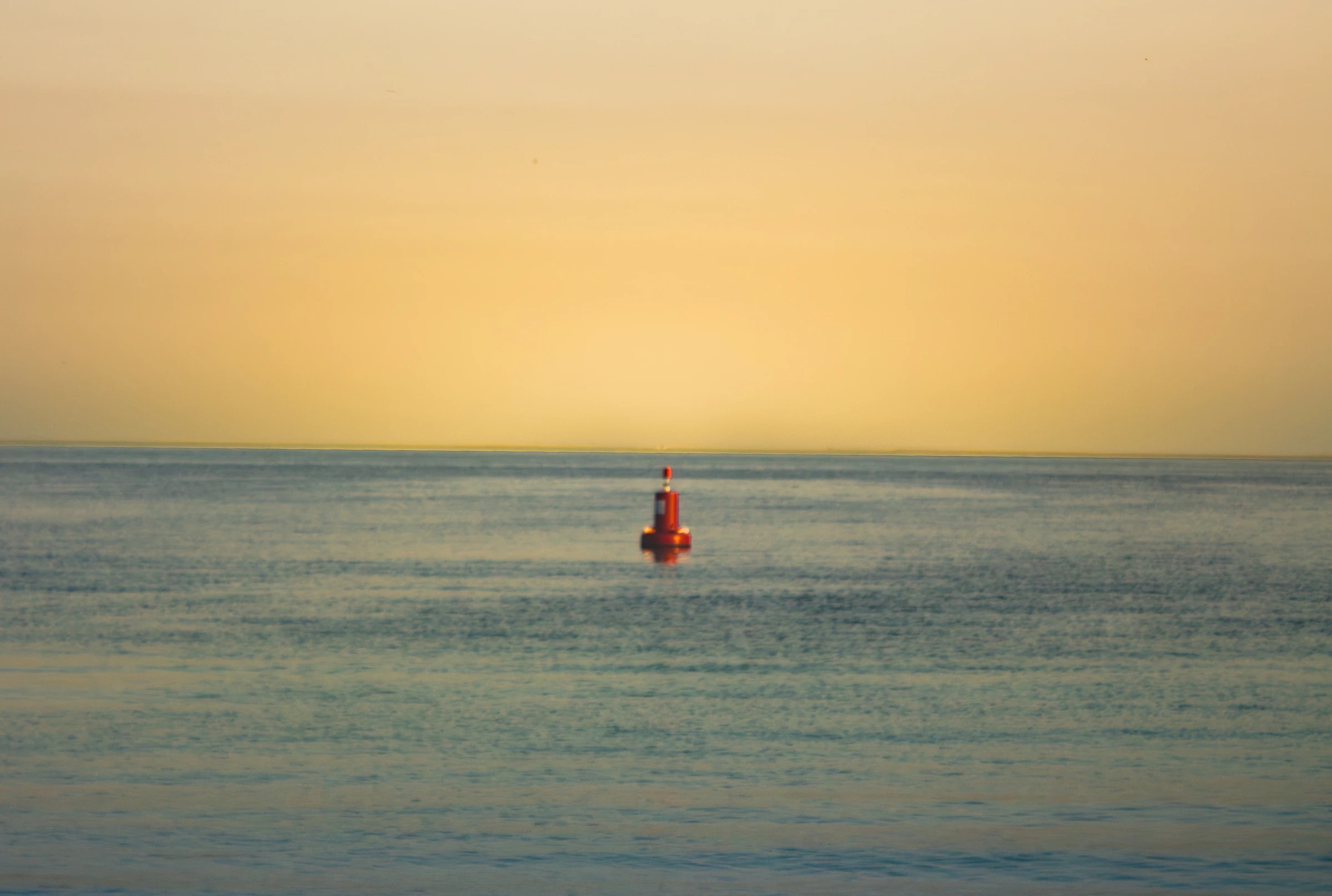 A red buoy on a quiet sea beneath a warm golden sky