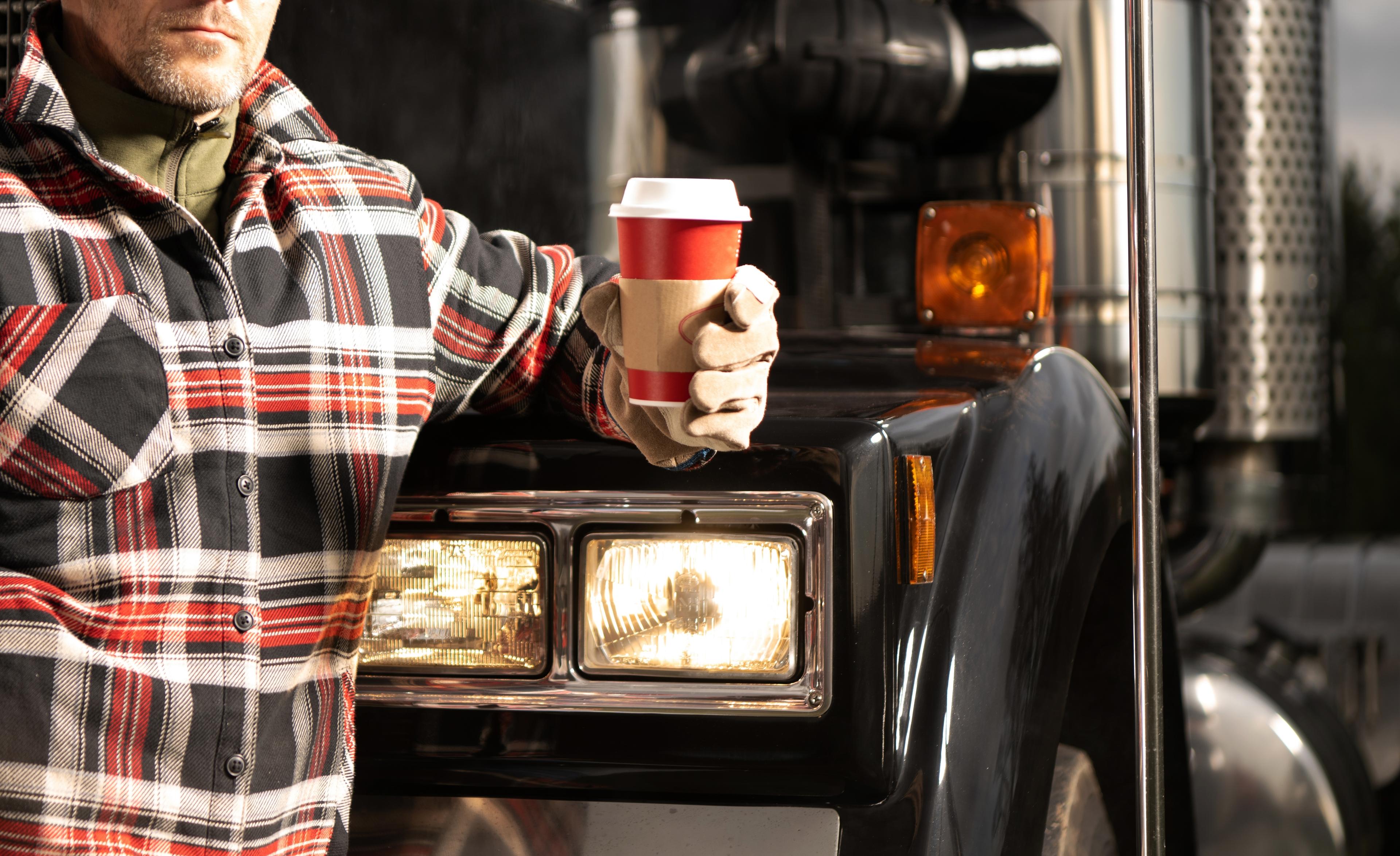 A man standing in front of a truck holding a coffee