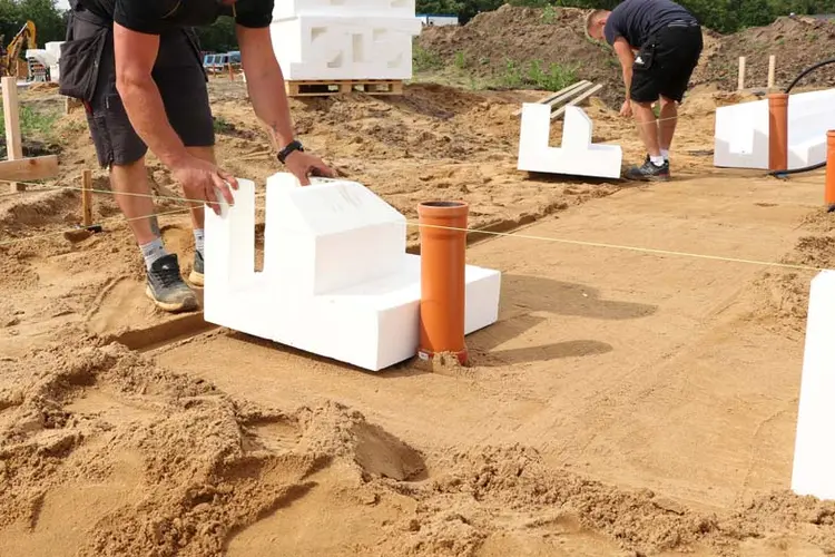 Foto af betonentreprenør i gang med at lægge funderingselement ud på sandpude. De lette elementer lægges med håndkraft så man sparer brændstof og letter arbejdet