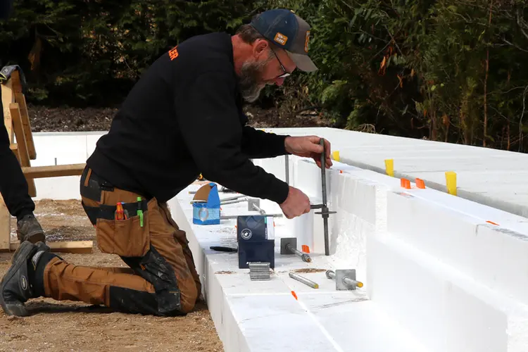 Håndværker i gang med at samle skruefundamenternes toppe til fundering på blød byggegrund