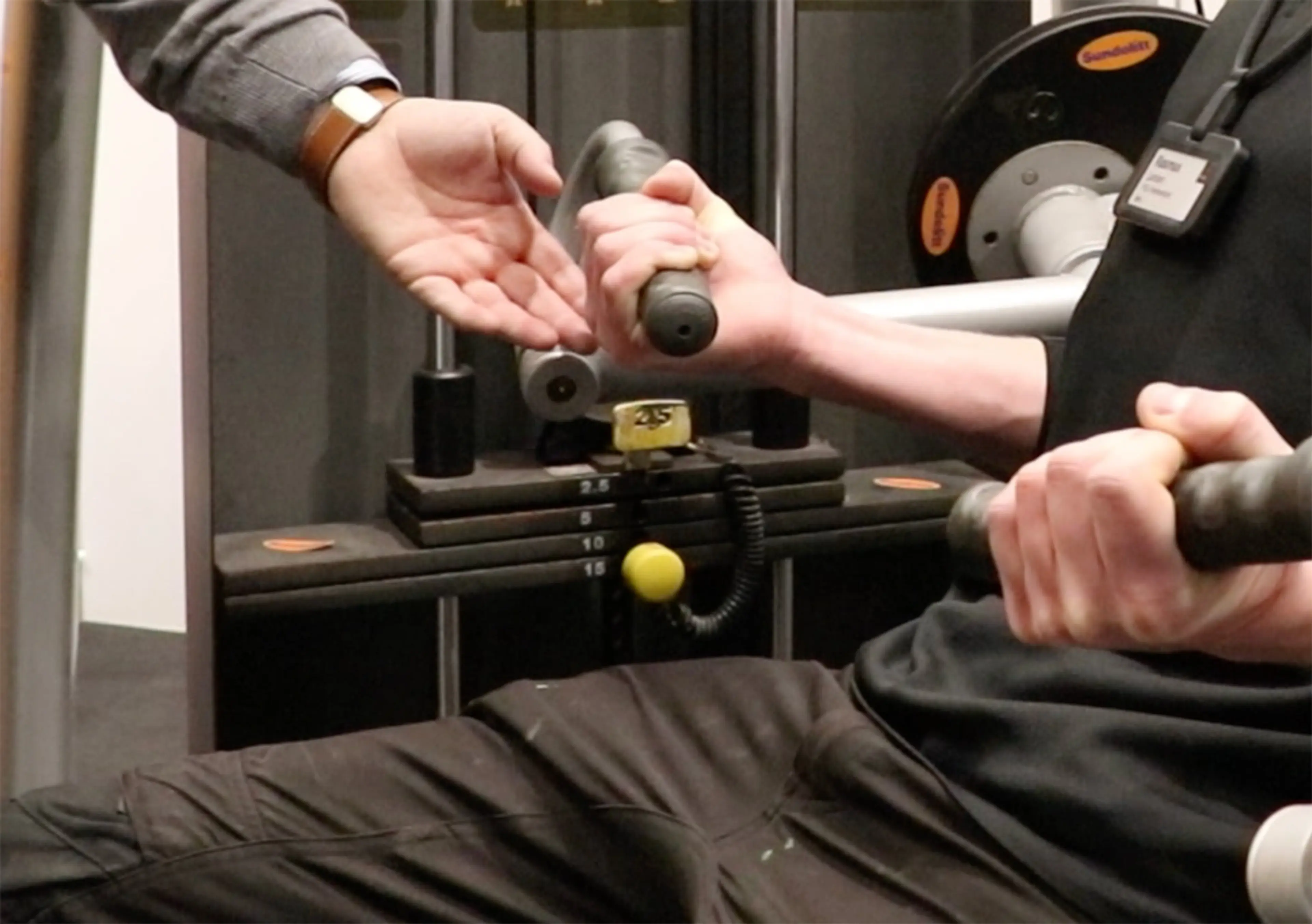 Håndværker sidder i en biceps curl på Byggerimessen 2025. En hånd minder håndværkeren om, at han skal holde spændet.