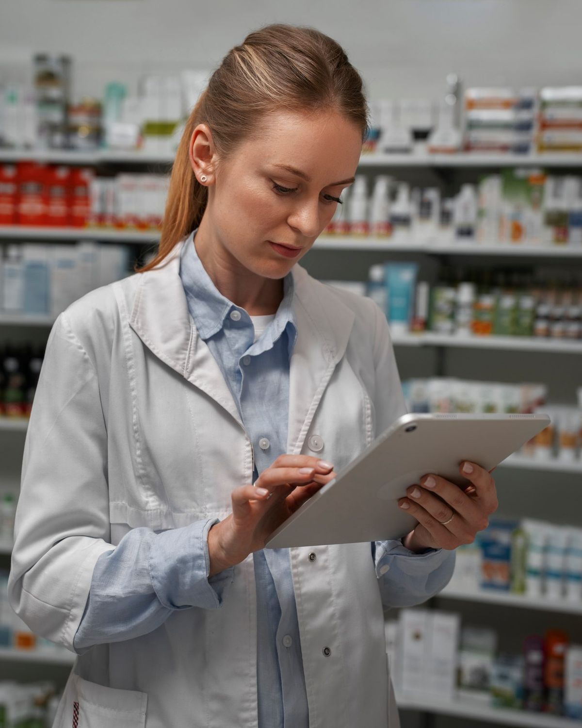 Pharmacist in a white coat using a tablet among stocked pharmacy shelves — Global Email Lists Email List of Pharmacies