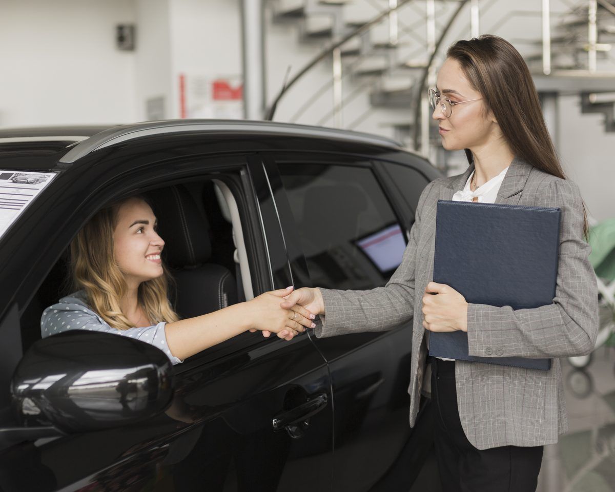 Car dealership saleswoman shaking hands with a customer at the showroom