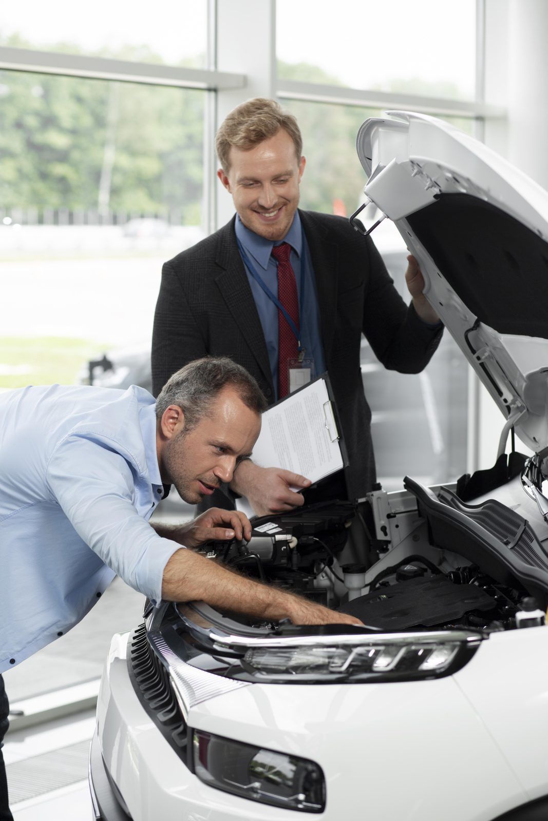 Car dealership salesperson inspecting a vehicle engine with a customer