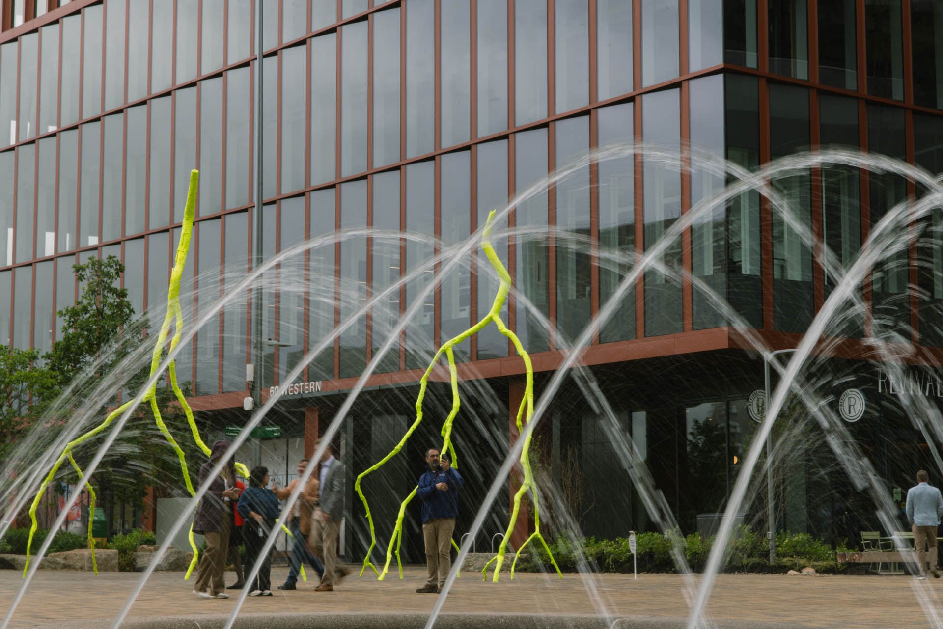 The image shows the monumental dayglo-yellow bronze sculptures titled “sublime light” and “blissful light” by artist Ugo Rondinone, on view at the Harvard Enterprise Research Campus in Boston.