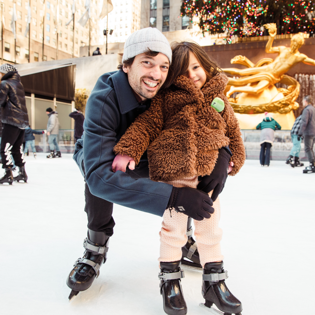 A father and daughter posing for a photo at The Rink at Rockefeller Center