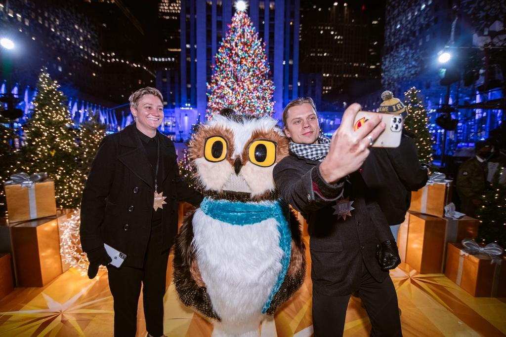Two people take a selfie with Roxy the Owl at the 2021 Rockefeller Center Tree Lighting