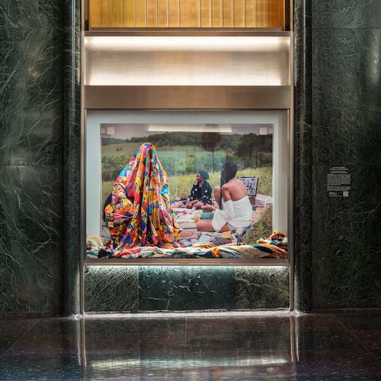 Person covered in a multi-colored quilt as part of artist Basil Kincaid's Art in Focus exhibit at Rockefeller Center