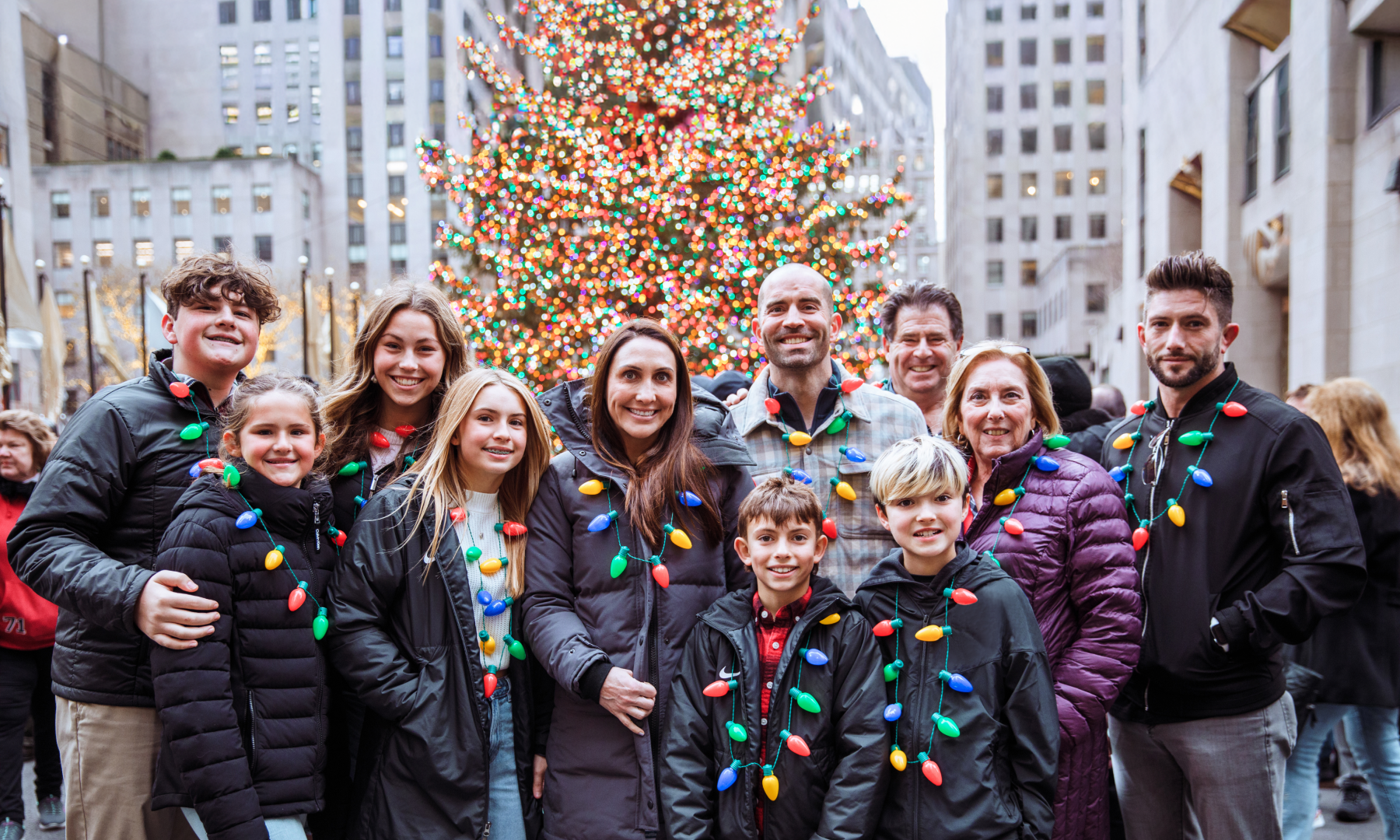 A family of 11 posing for a photo in front of the Rockefeller Center Christmas Tree