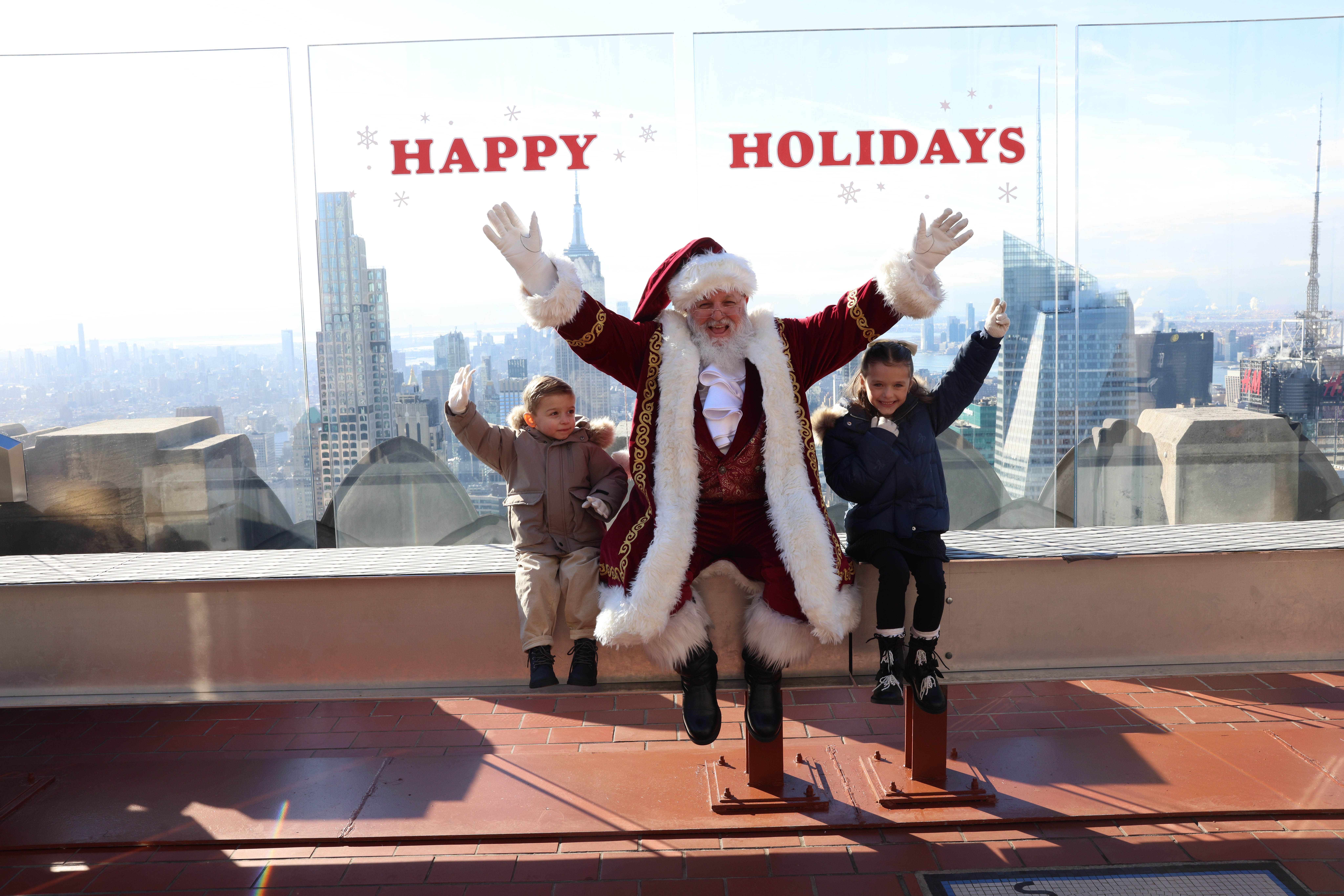 Two children taking a photo with Santa on The Beam at Top of the Rock