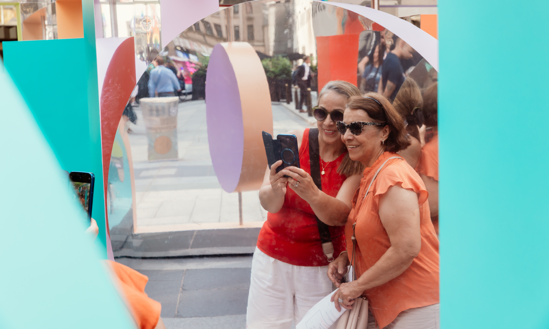Two women taking a photo in front of "Reflection Point," a public art piece by artists Wade and Leta