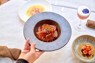 Holding a plate of tuna tartare over a white tablecloth with a pink cocktail