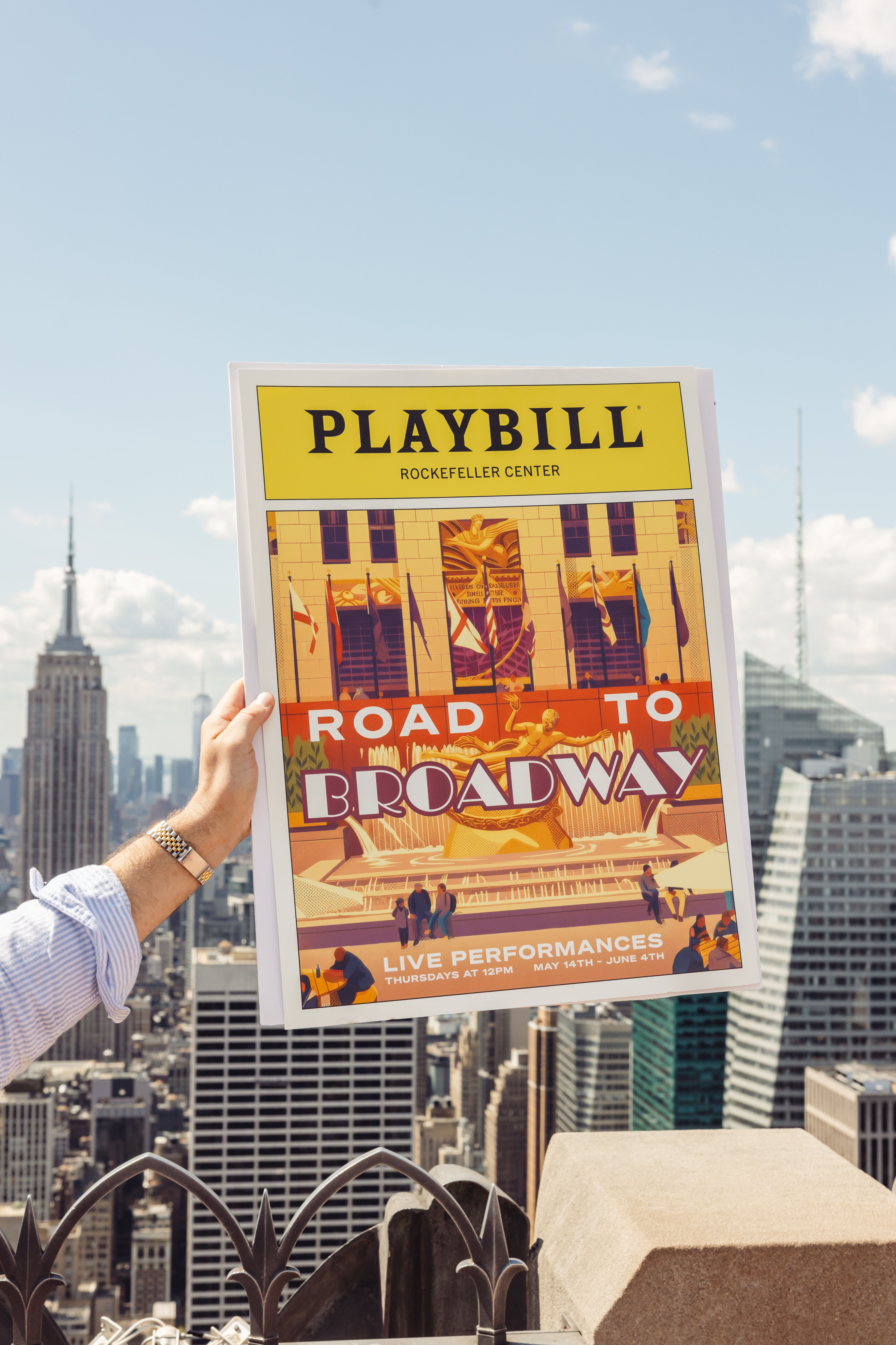 person holding up a Road to Broadway poster at Top of the Rock
