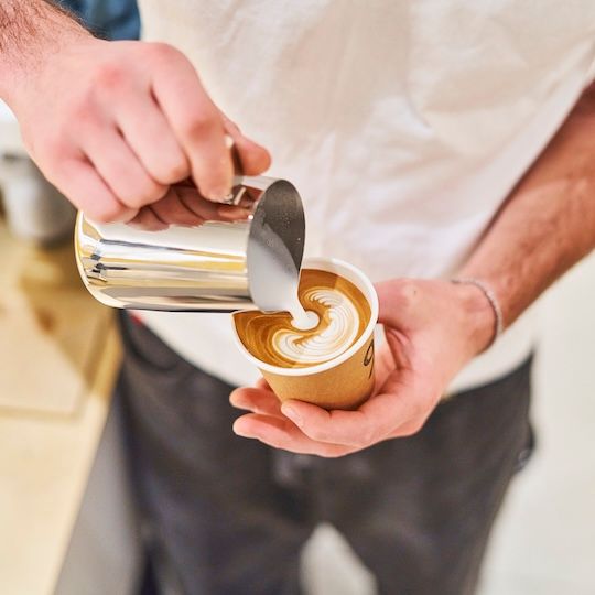 % Arabica employee pouring milk into a cup of coffee