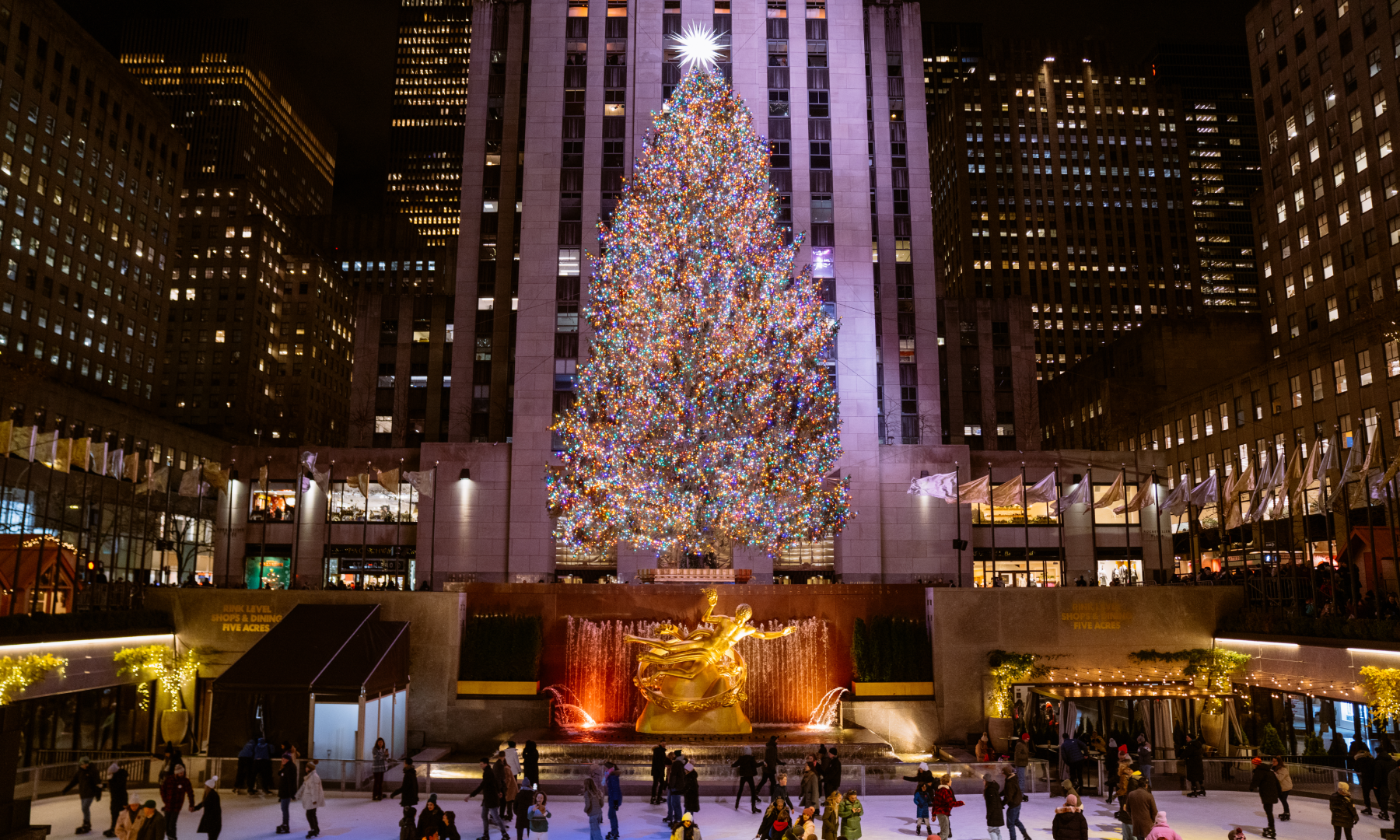 A large group of people ice skating under the Rockefeller Center Christmas Tree at The Rink