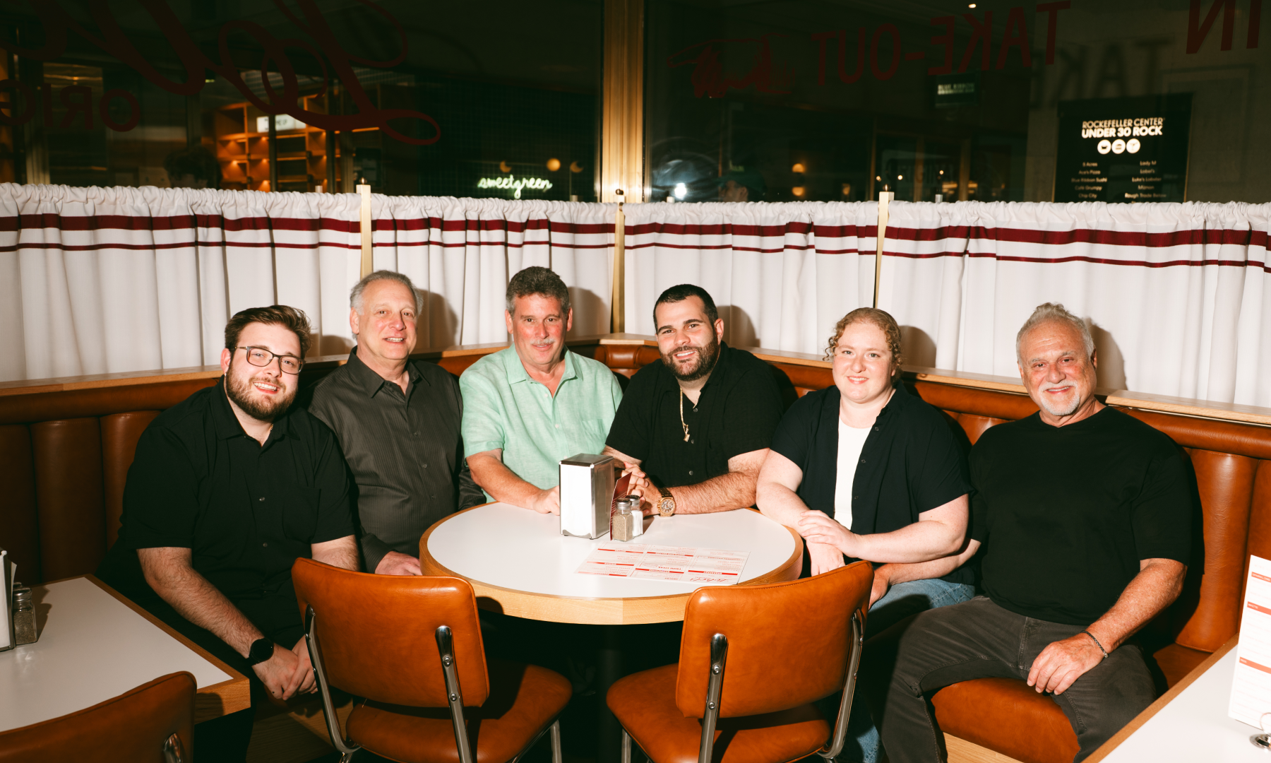 Six members of the Lobel family gathered around a table at Lobel's Original at Rockefeller Center