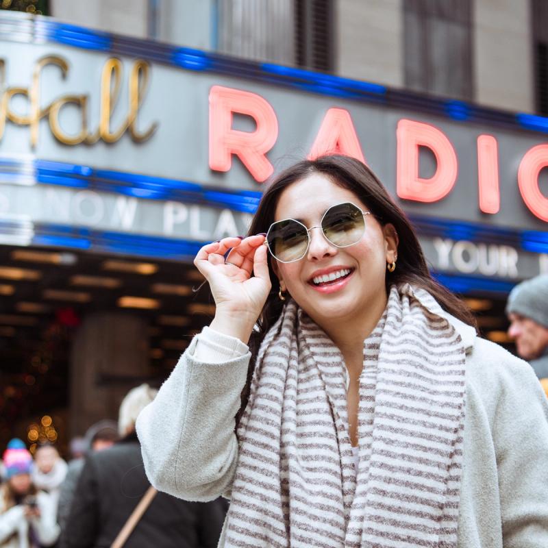 Girl with dark hair wearing the Celia Sunglasses in Mint by Warby parker in front of radio city music hall