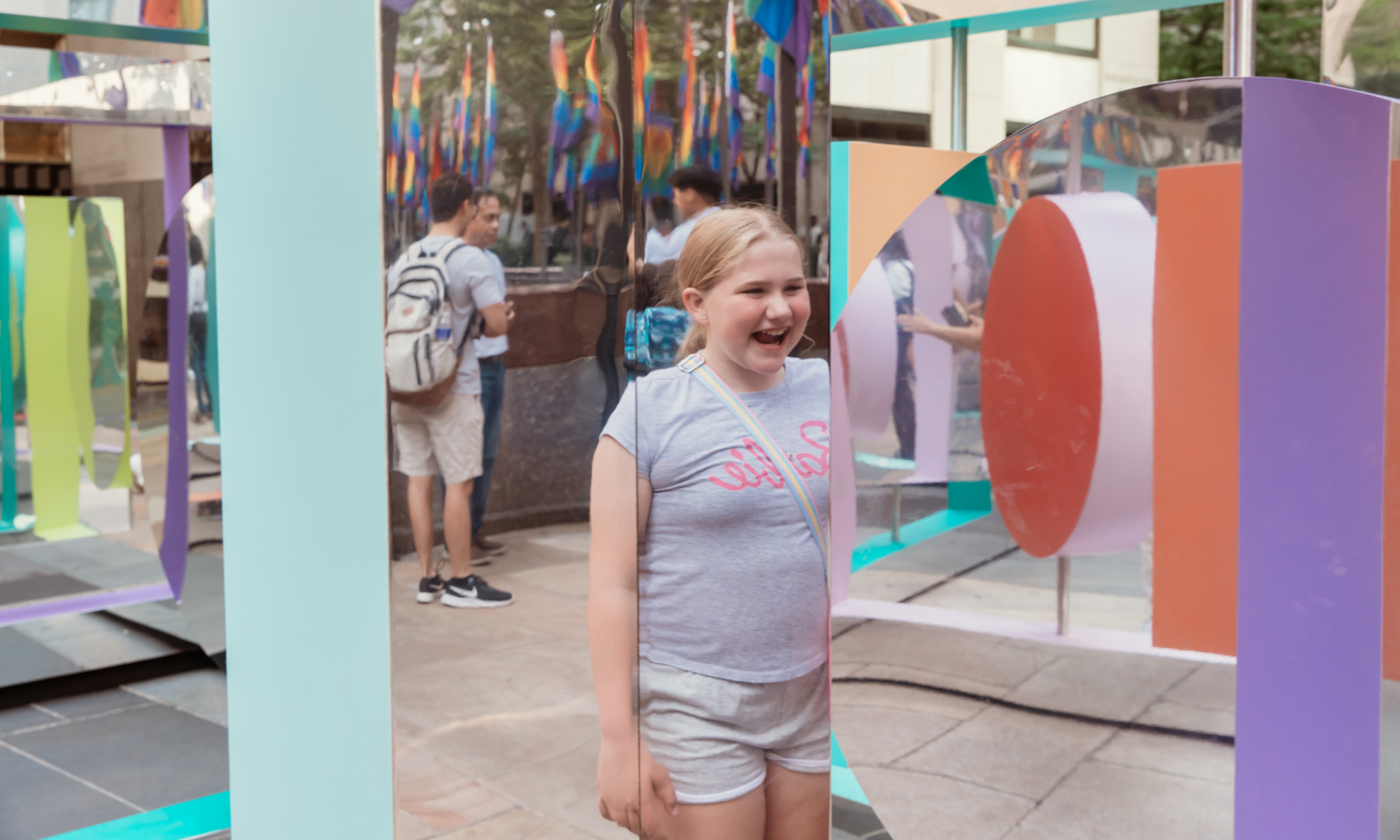 A child smiling at her reflection in front of "Reflection Point" on Center Plaza