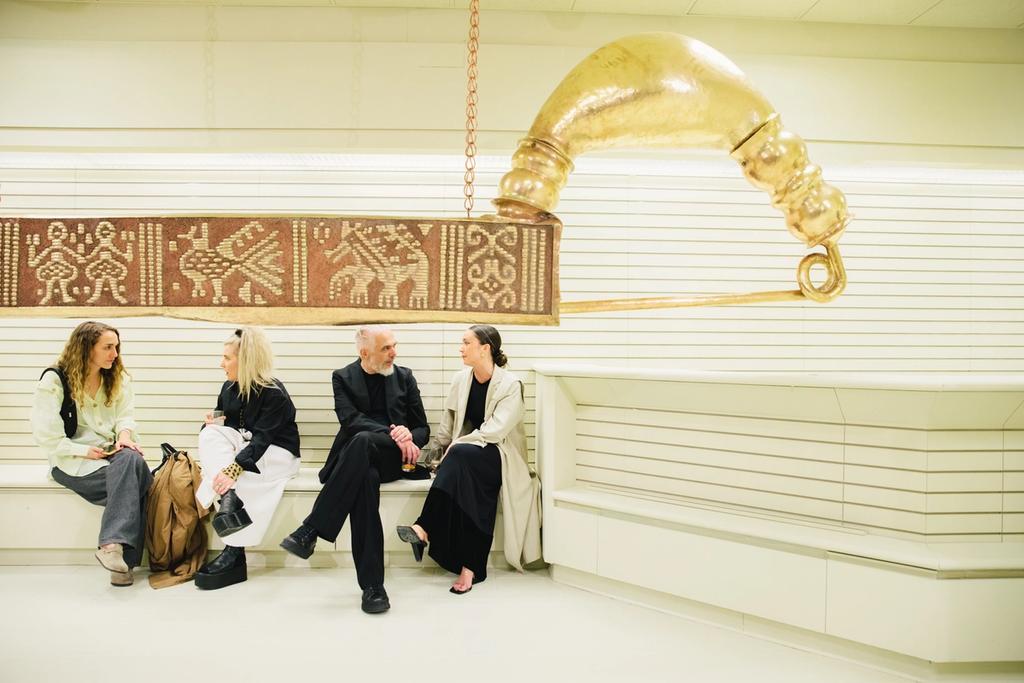 People sitting next to a golden hanging sculpture at MASA's exhibition at Rockefeller Center