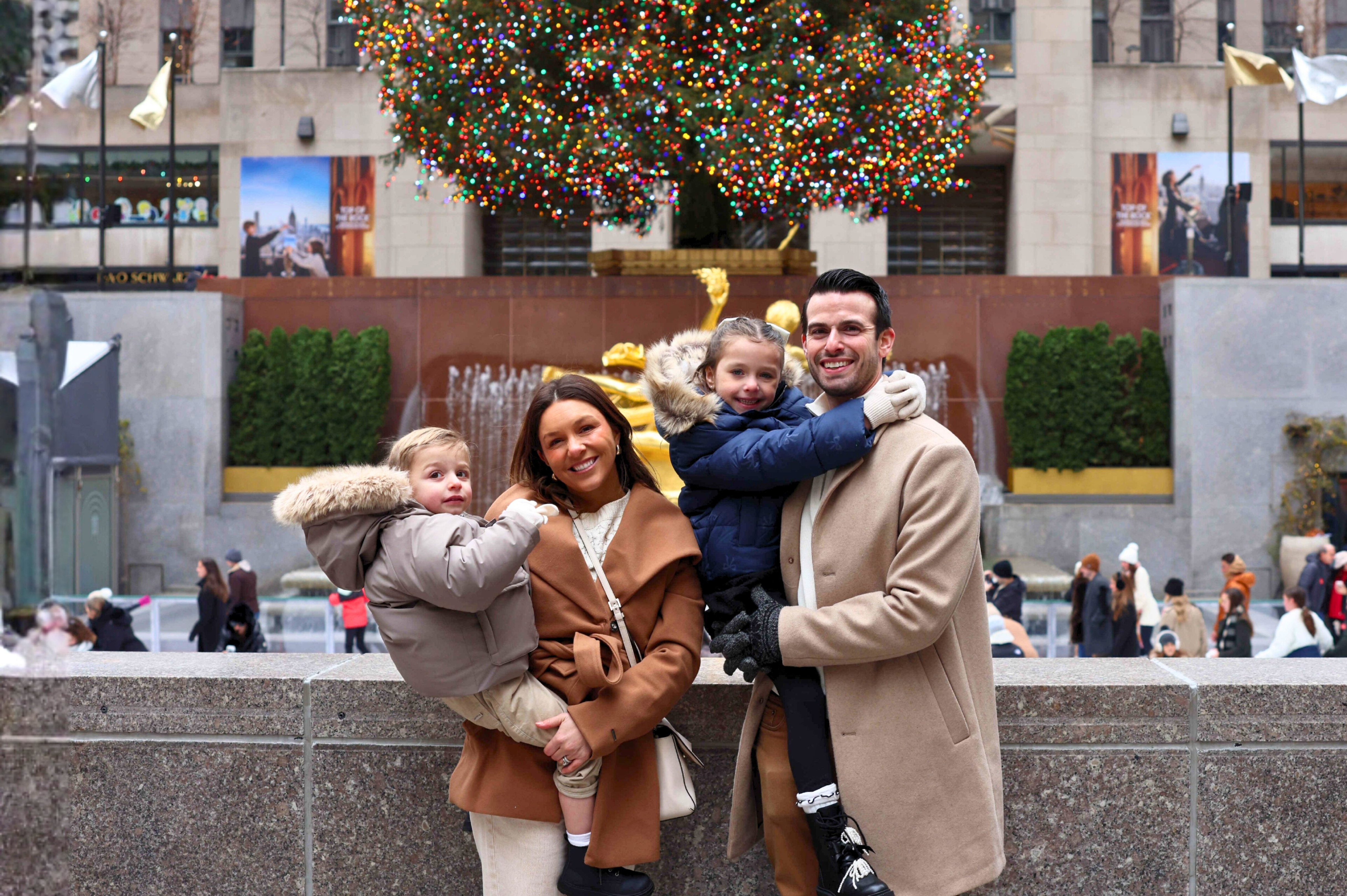 Family smiling in front of the rockefeller center christmas tree