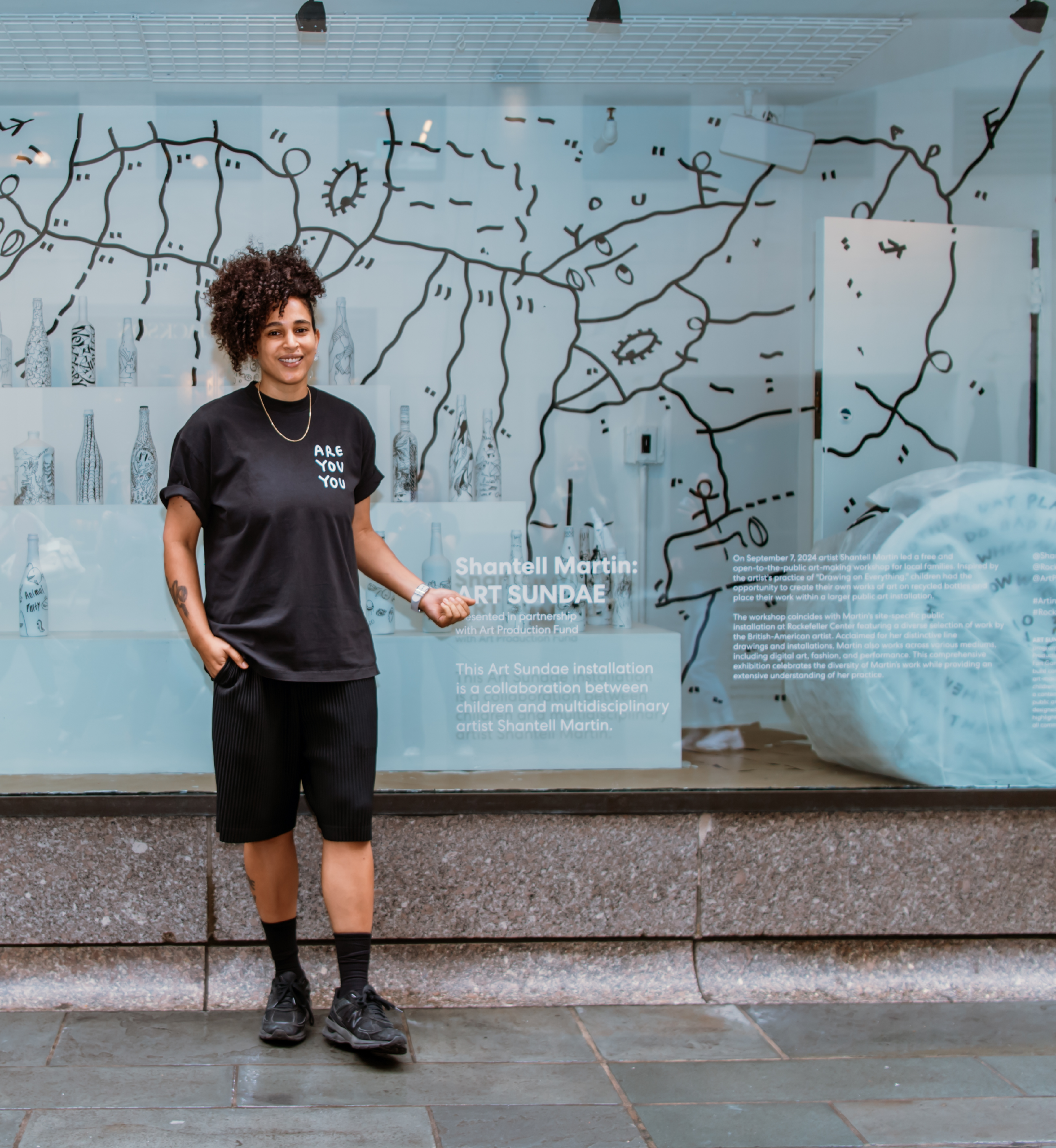 Artist Shantell Martin posing in front of a window display of her work at Rockefeller Center