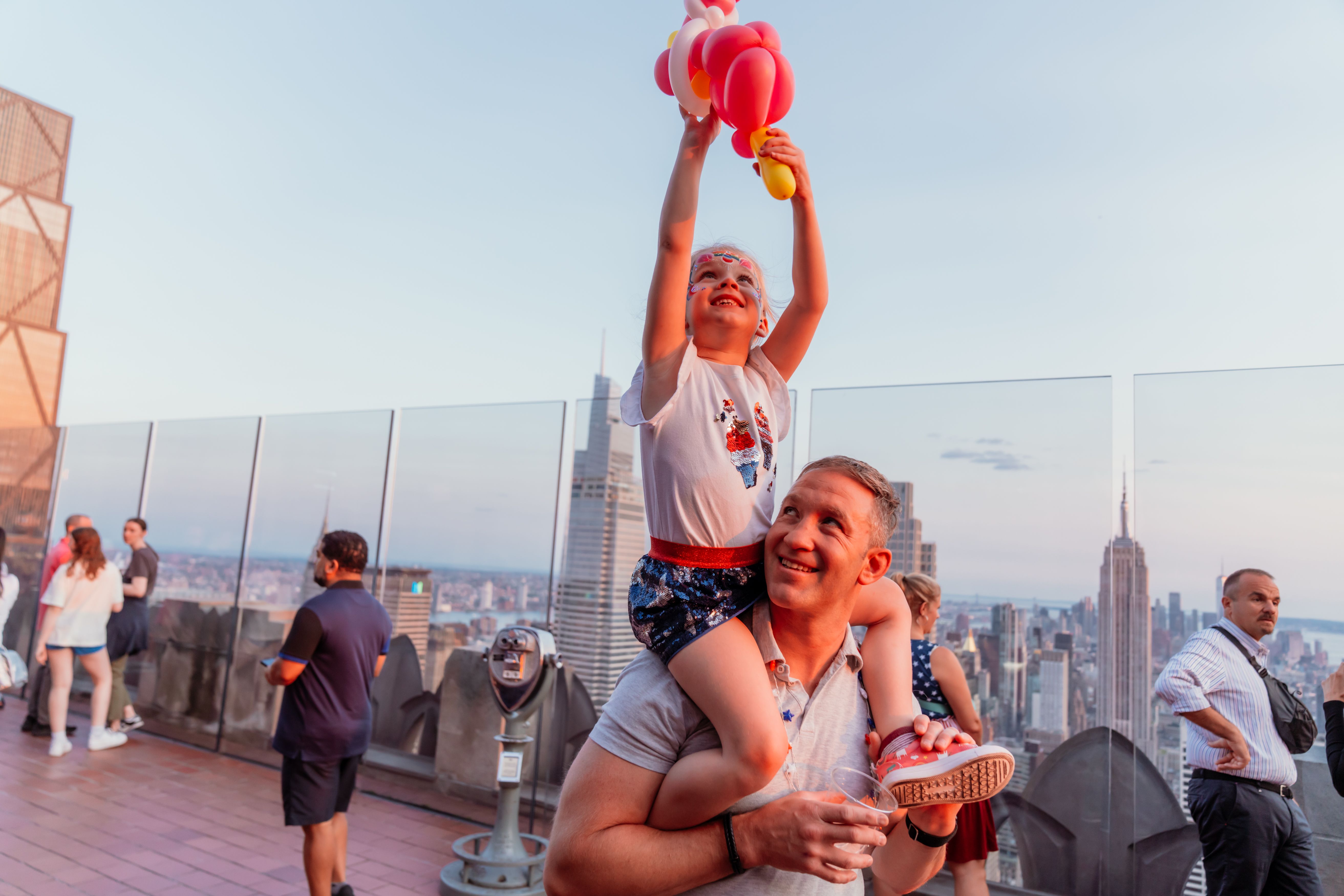 A parent carrying their child on their shoulders at Top of the Rock Observation Deck on the Fourth of July