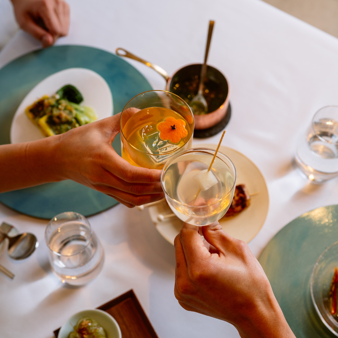 Two hands holding two cocktails from NARO at Rockefeller Center