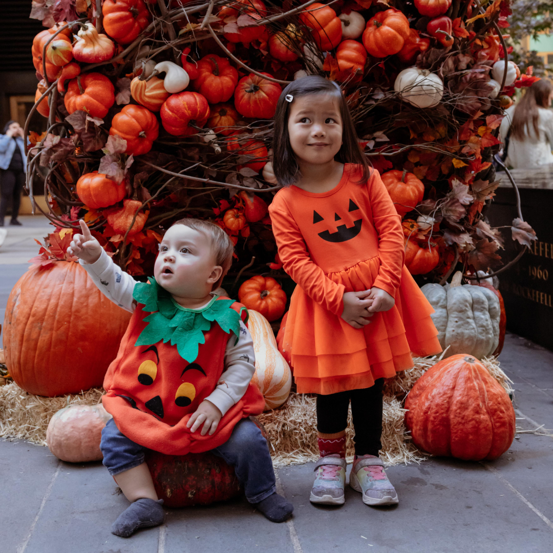 A baby and toddler posing in front of a pumpkin arch at Rockefeller Center