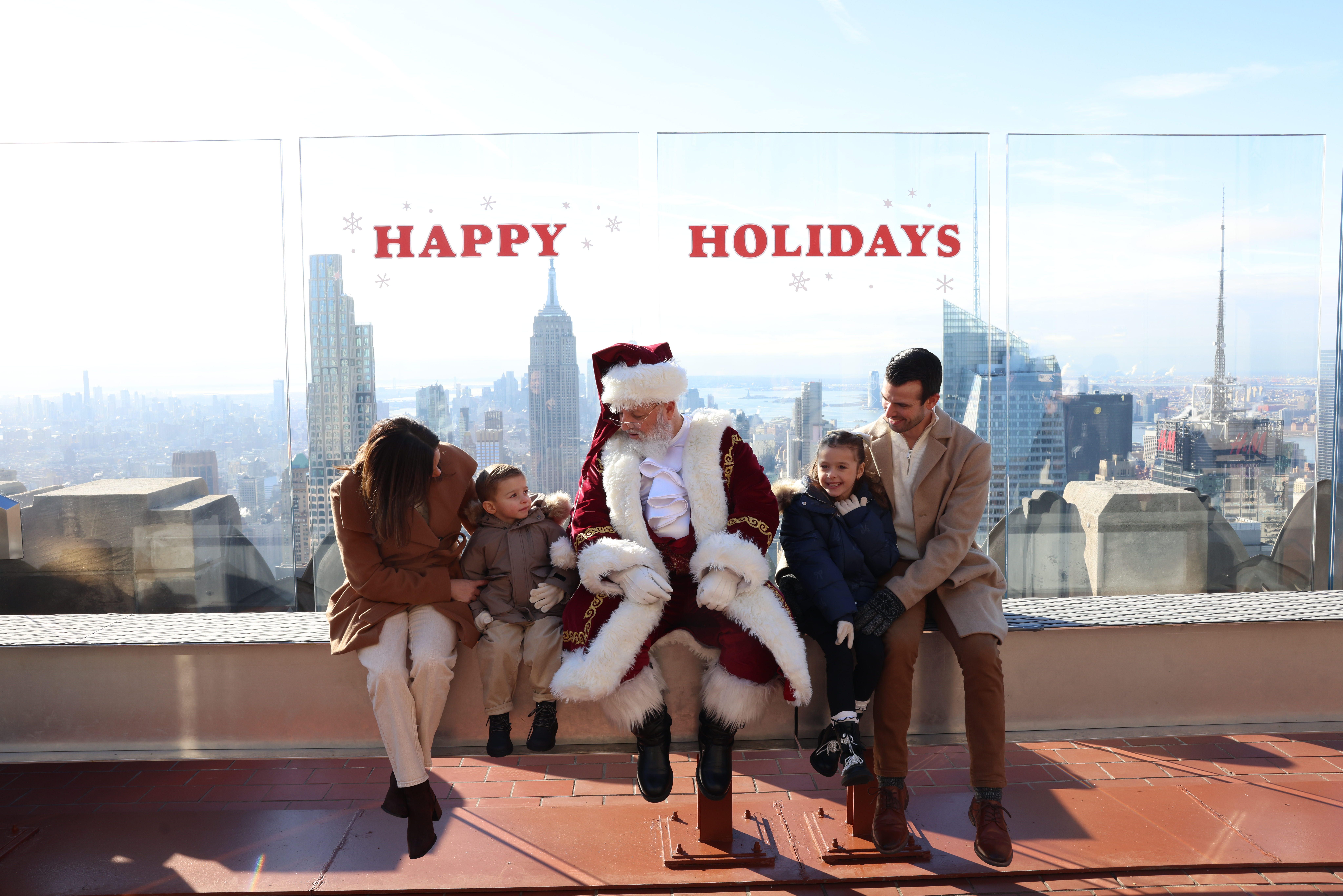 A family posing for a photo with Santa on The Beam at Top of the Rock