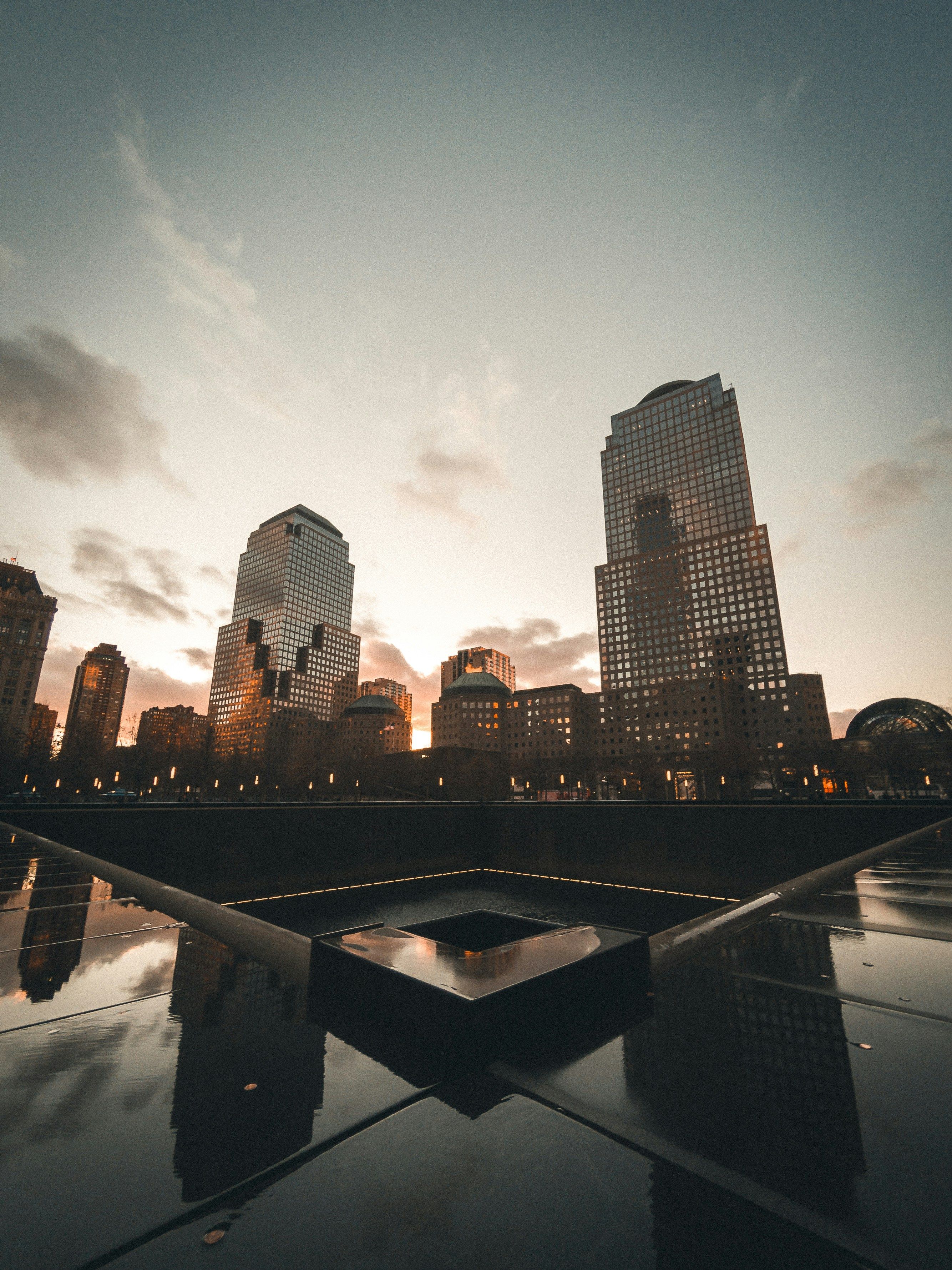 One of the 9/11 Memorial reflecting pools at sunset, with the World Trade Center site behind it.