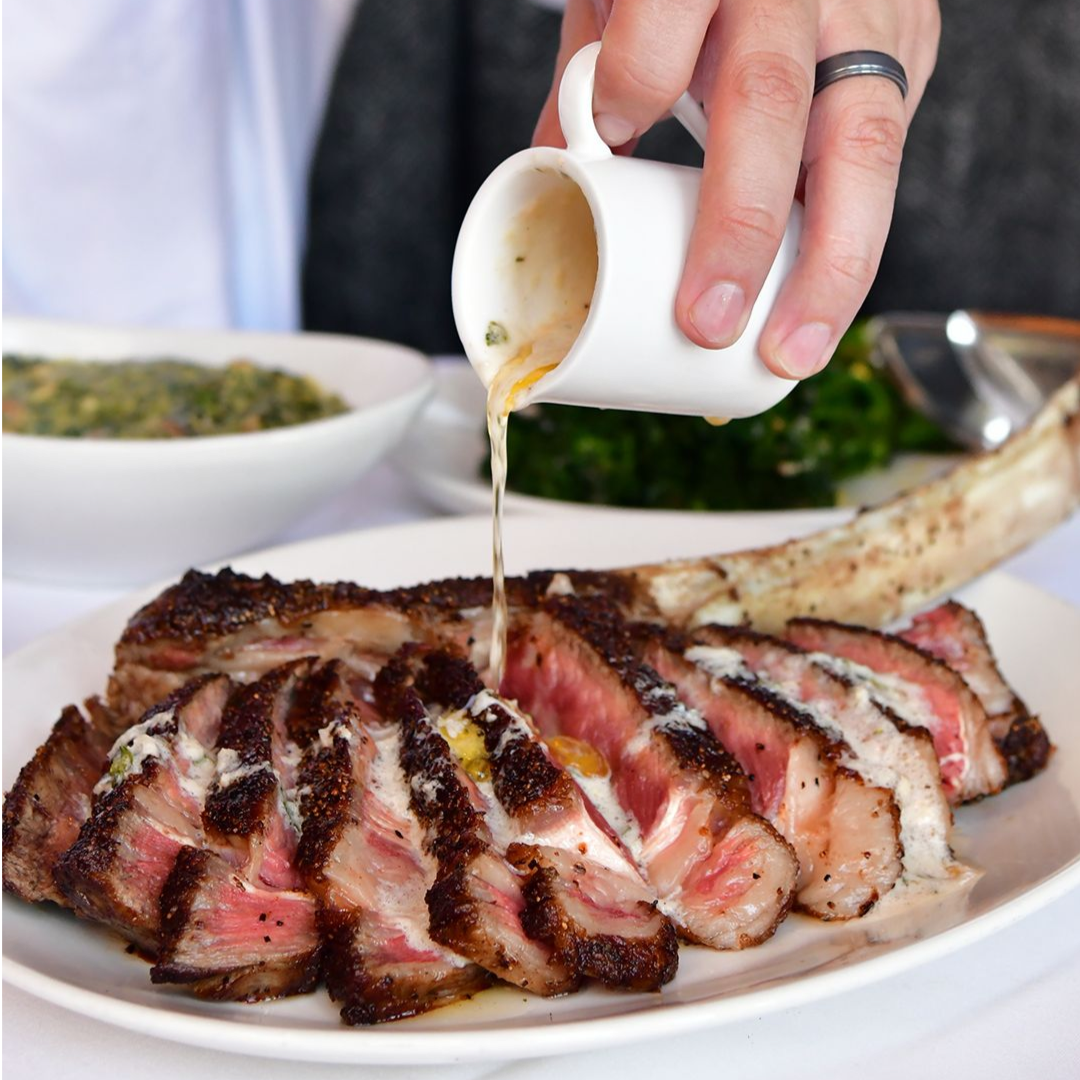 A hand pouring sauce on a steak from Del Frisco’s Double Eagle Steak House