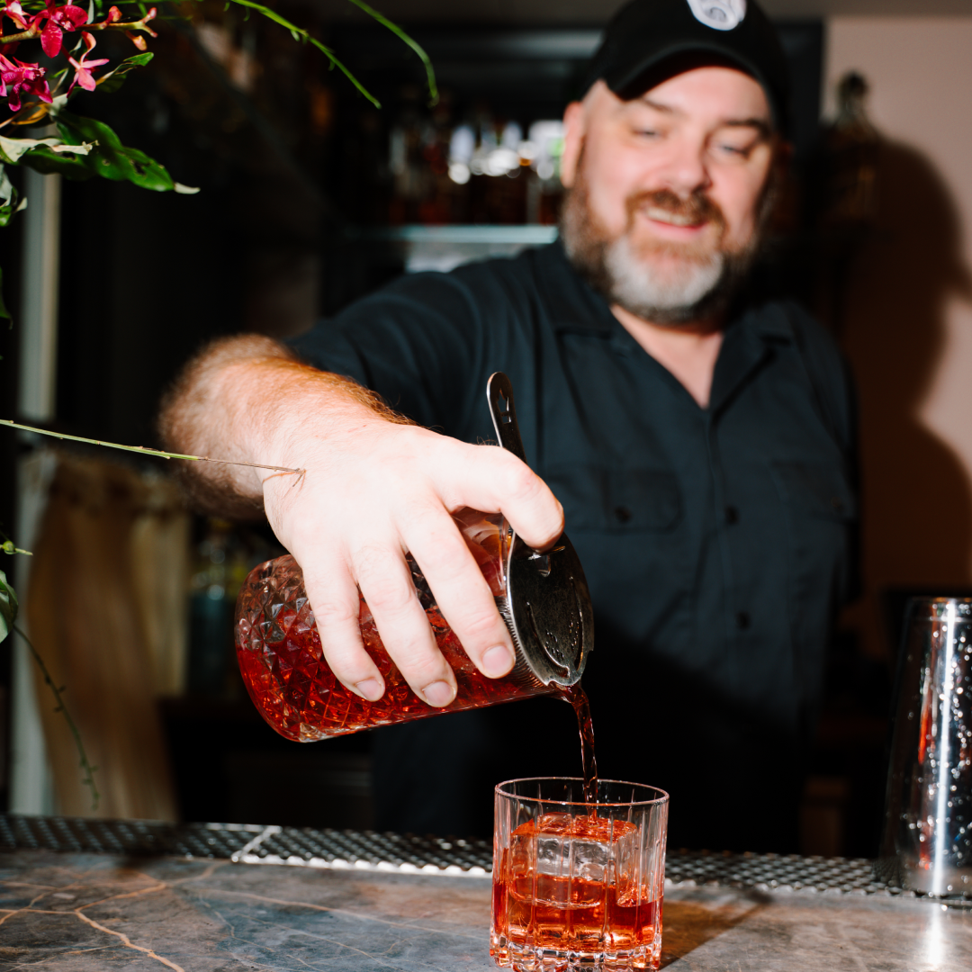 bartender pouring a beautiful red concoction through a strainer