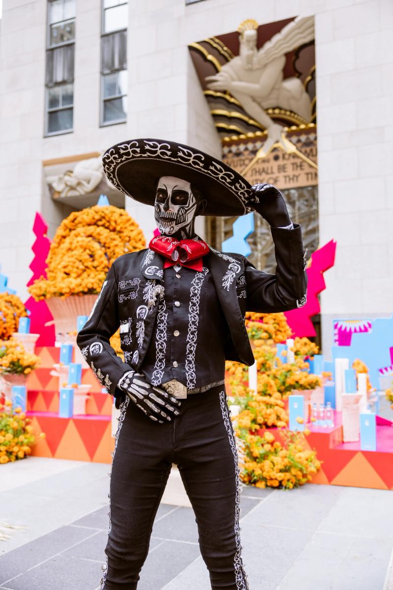 Man in Day of the Dead Catrina face paint standing in front of an ofrenda