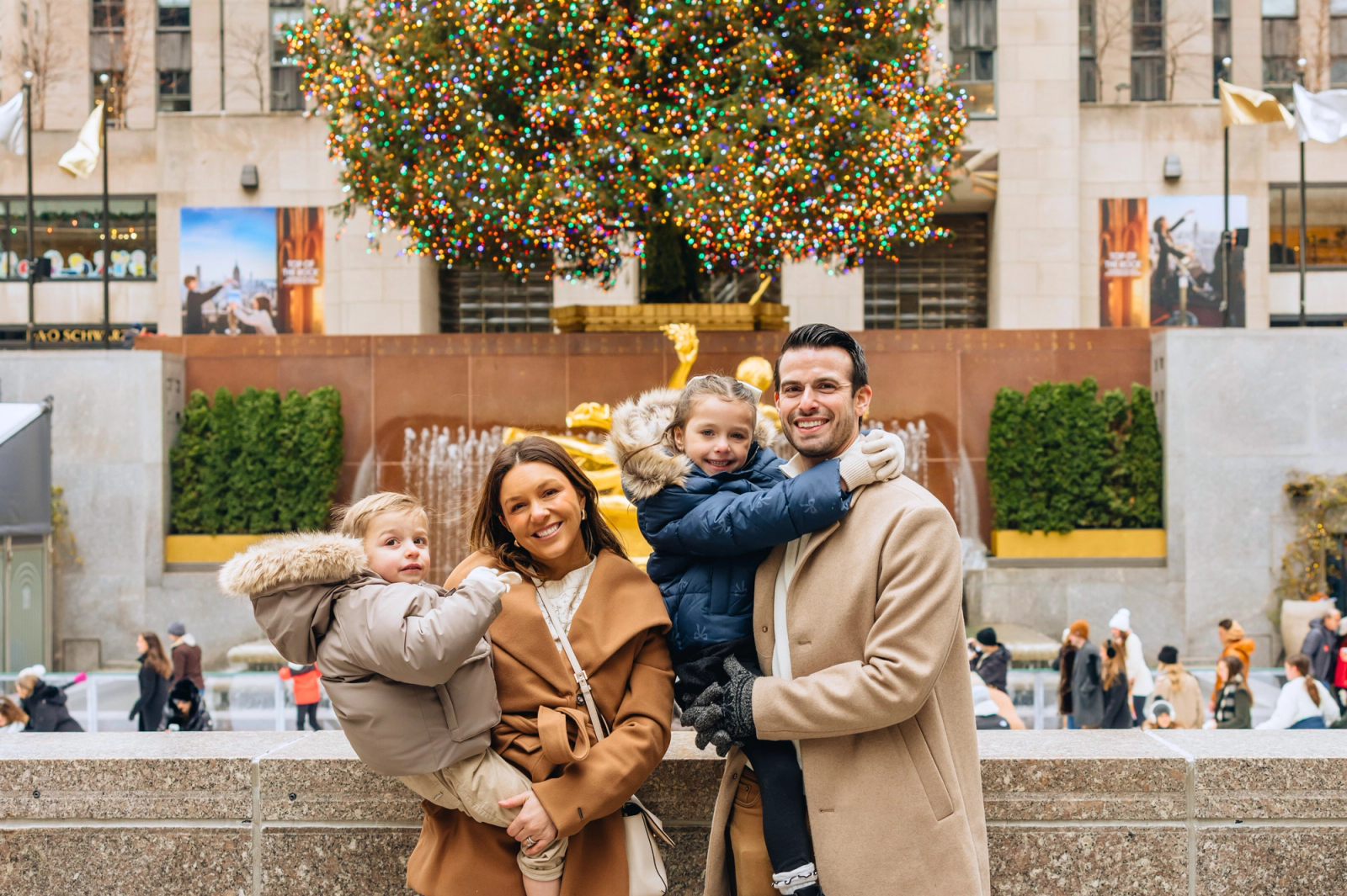 Family smiling in front of the rockefeller center christmas tree