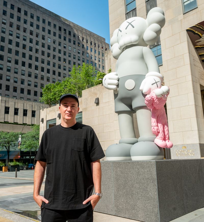 Artist KAWS stands in front of his sculpture SHARE on Center Plaza