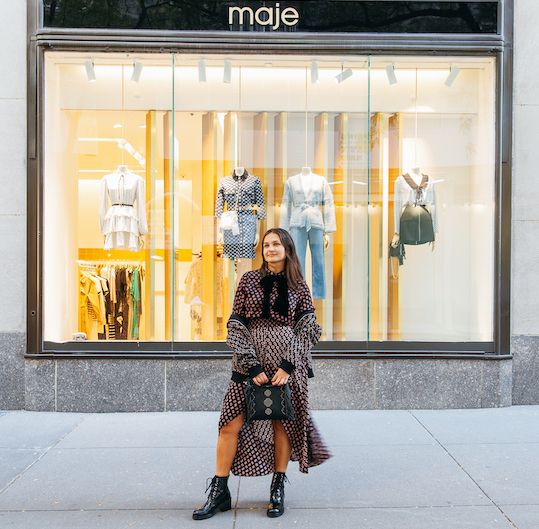 Woman standing in front of Maje in a matching skirt and blouse set