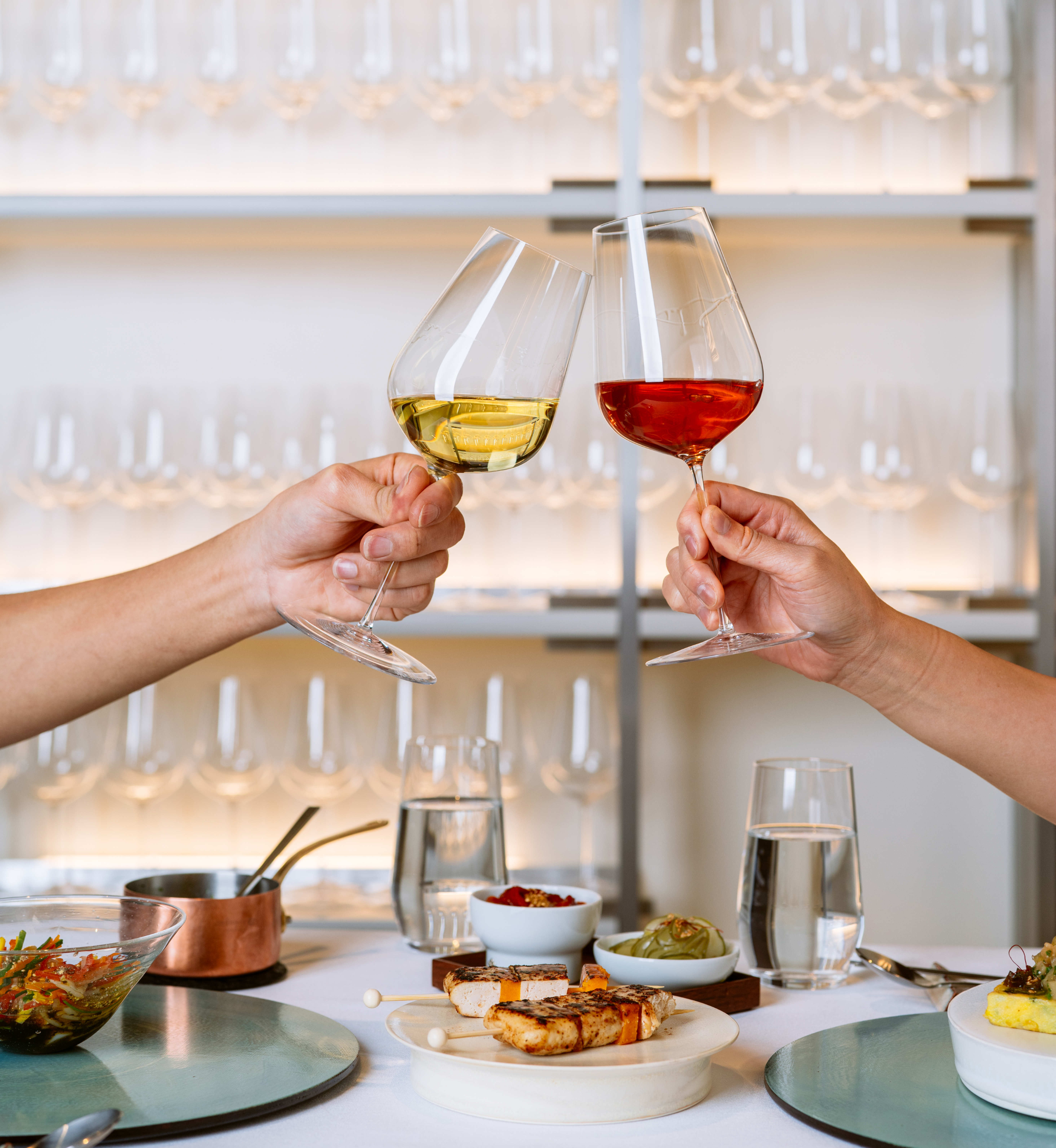 Two hands clinking glasses filled with wine at NARO at Rockefeller Center