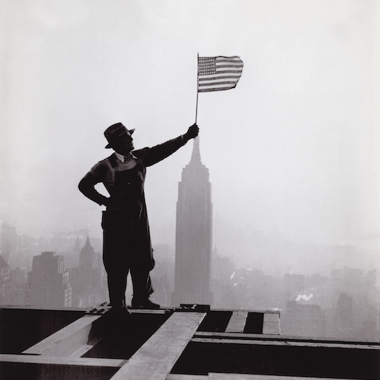Man holding an American flag while standing on a beam