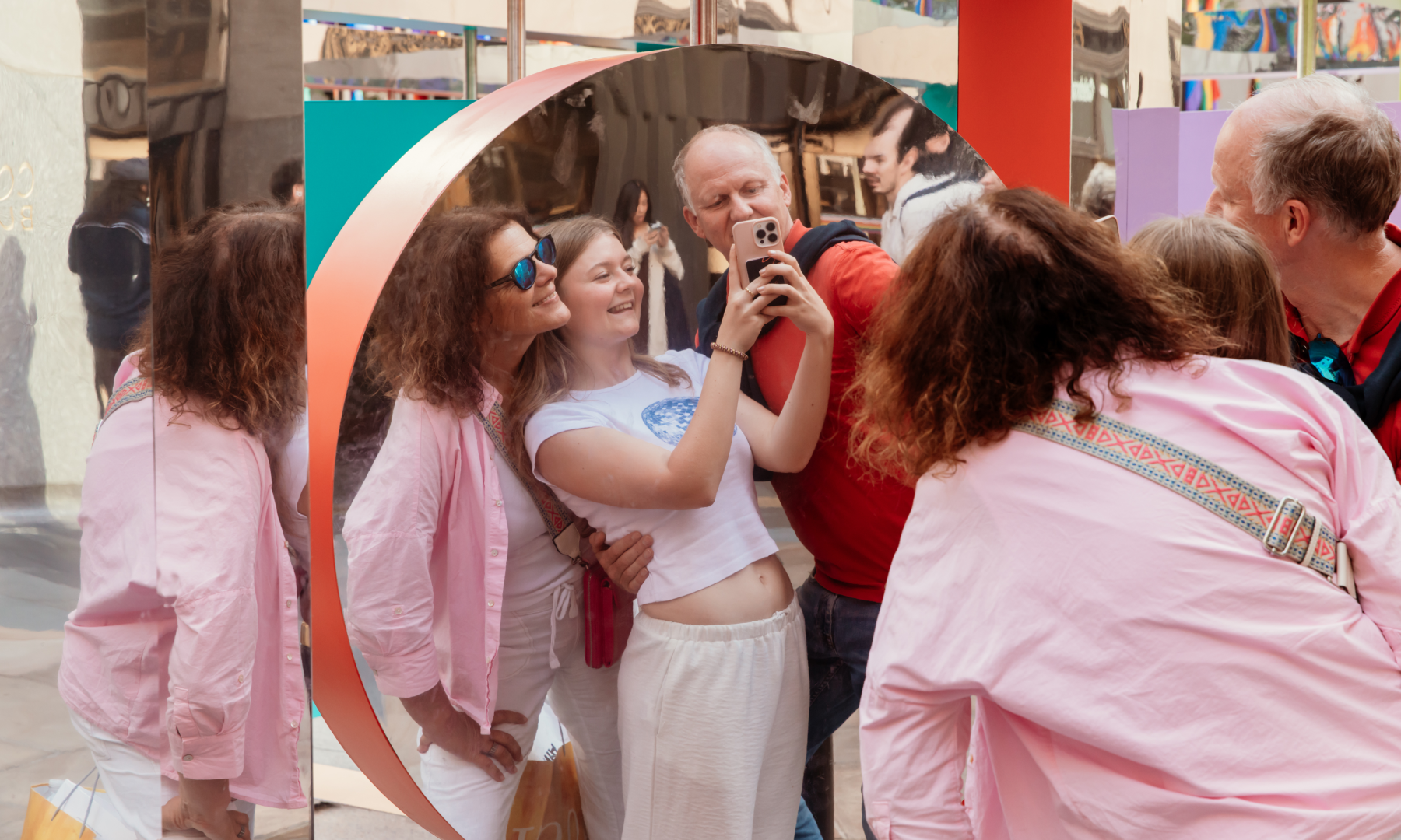 Two parents and their daughter taking a photo in front of Wade and Leta's "Reflection Point" sculpture