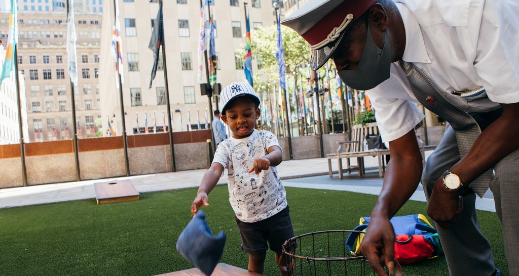 CJ playing cornhole with a toddler on the Rockefeller Center plaza 