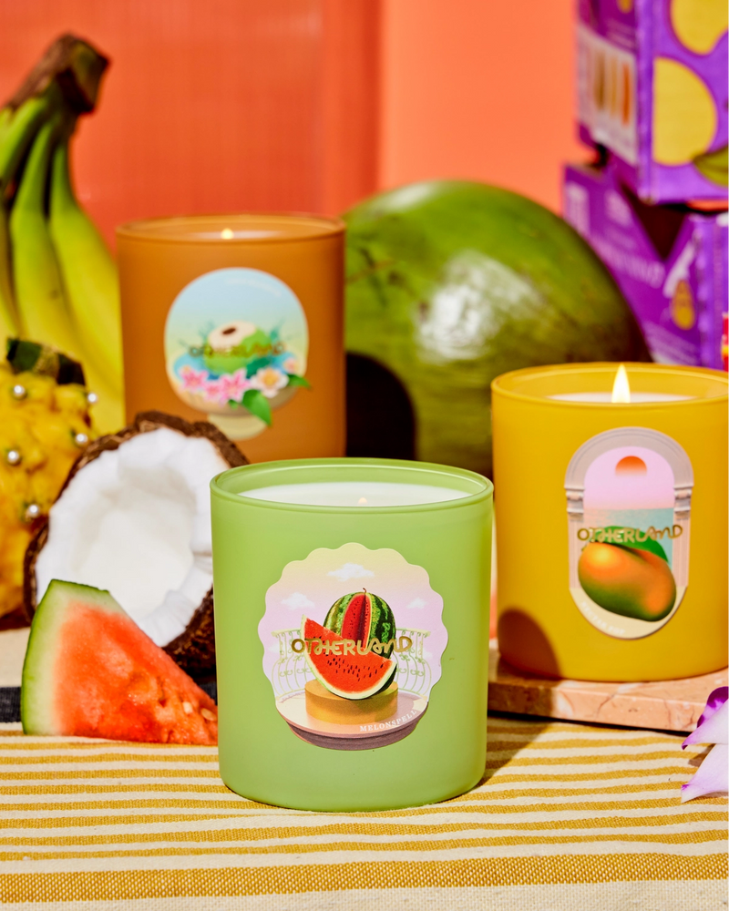 Colorful fruit scented candles on an orange backdrop with pieces of watermelon and coconut.