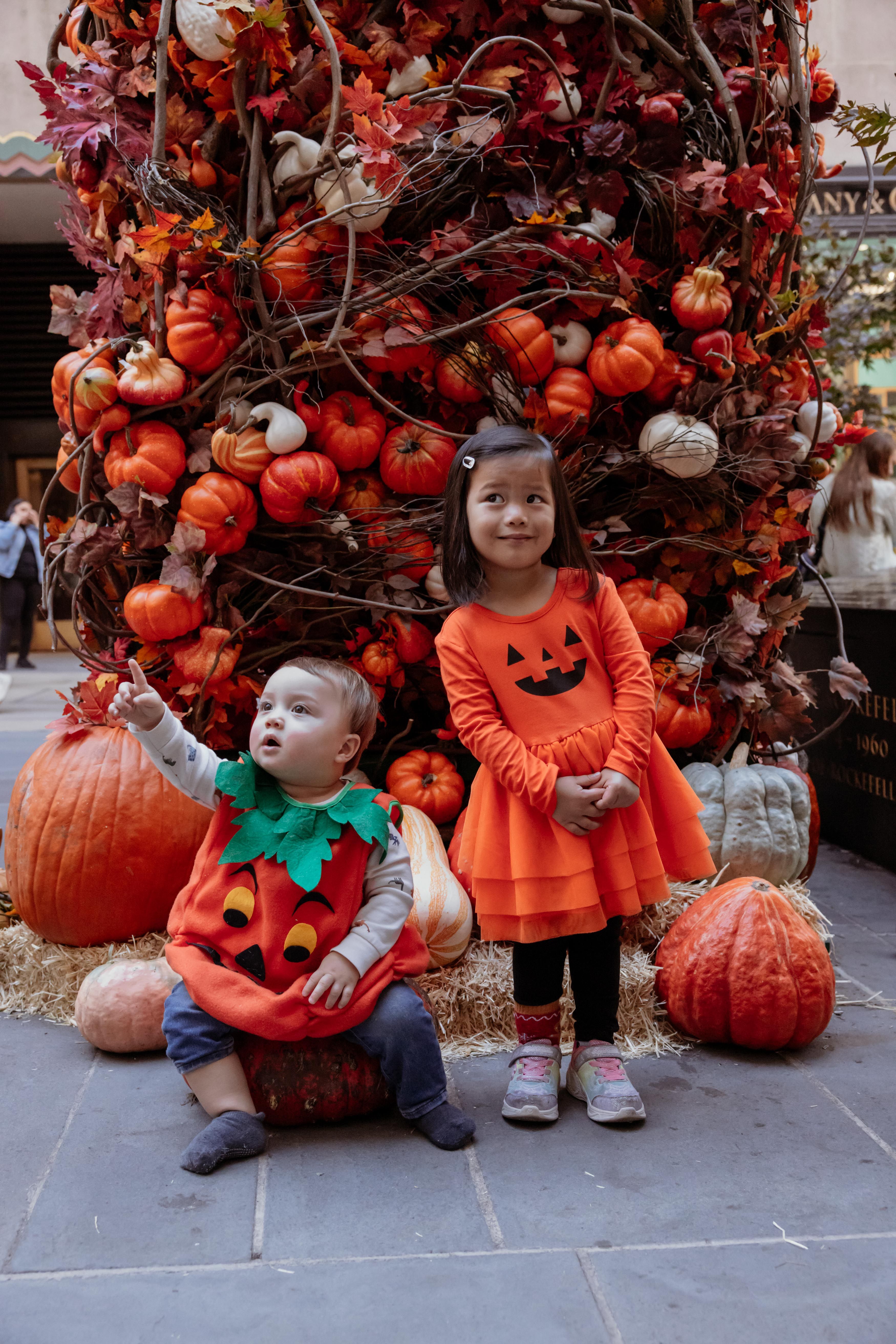 Two kids in Halloween costumes in front of a pumpkin arch 