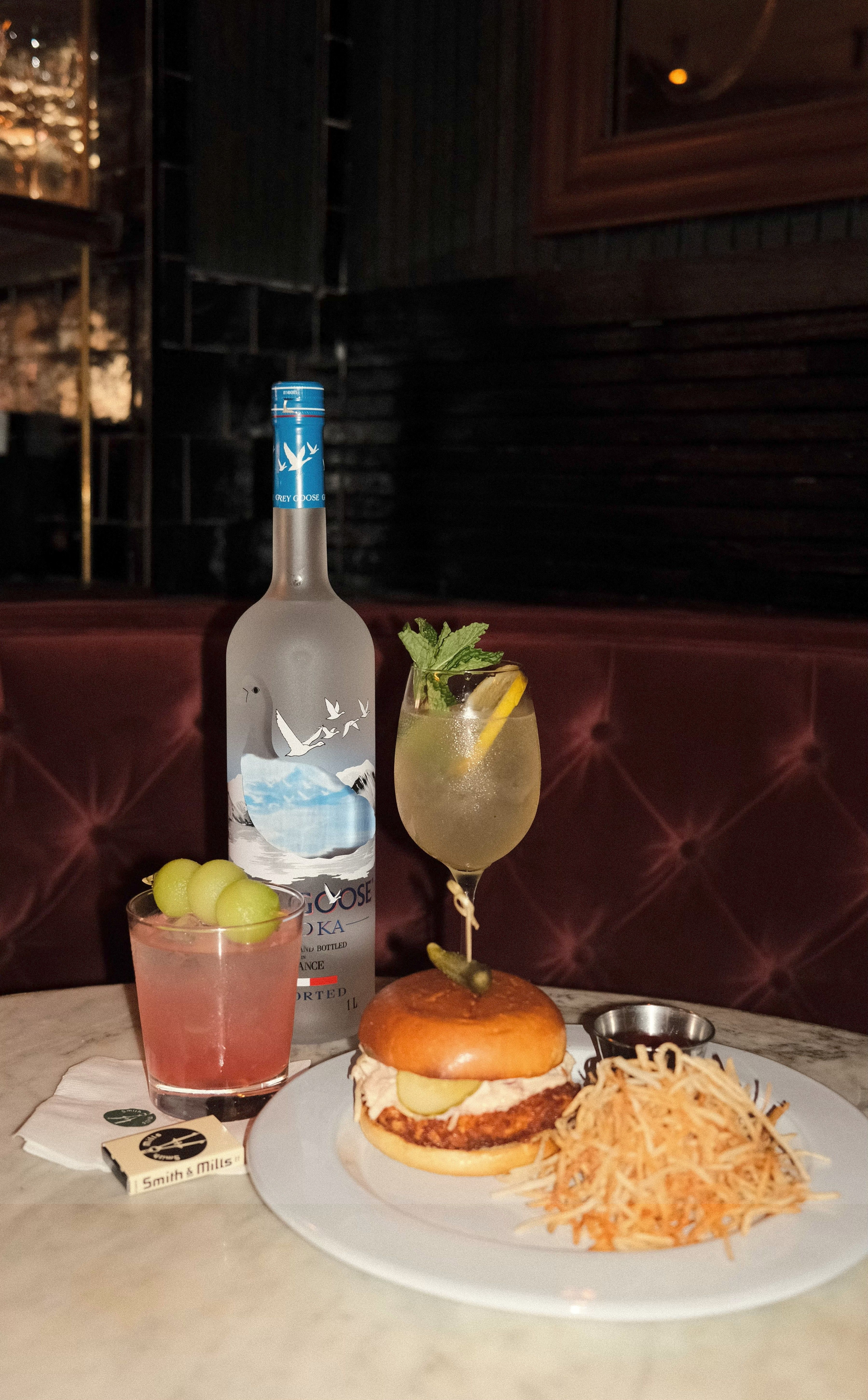 burger, fries, two cocktails and a bottle of grey goose vodka on a table